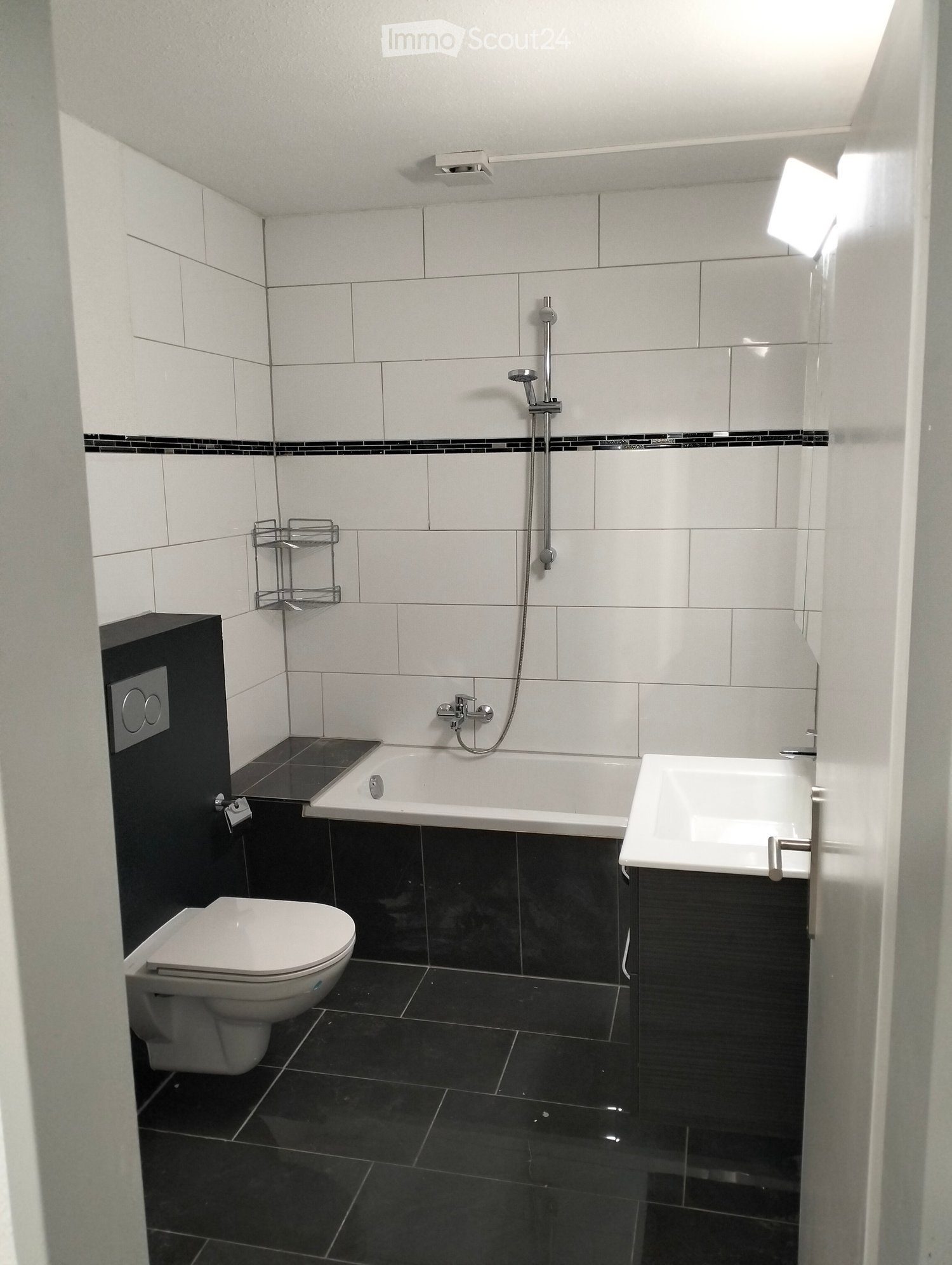 Modern bathroom with white tiles, black accents, bathtub, toilet, sink, and showerhead.