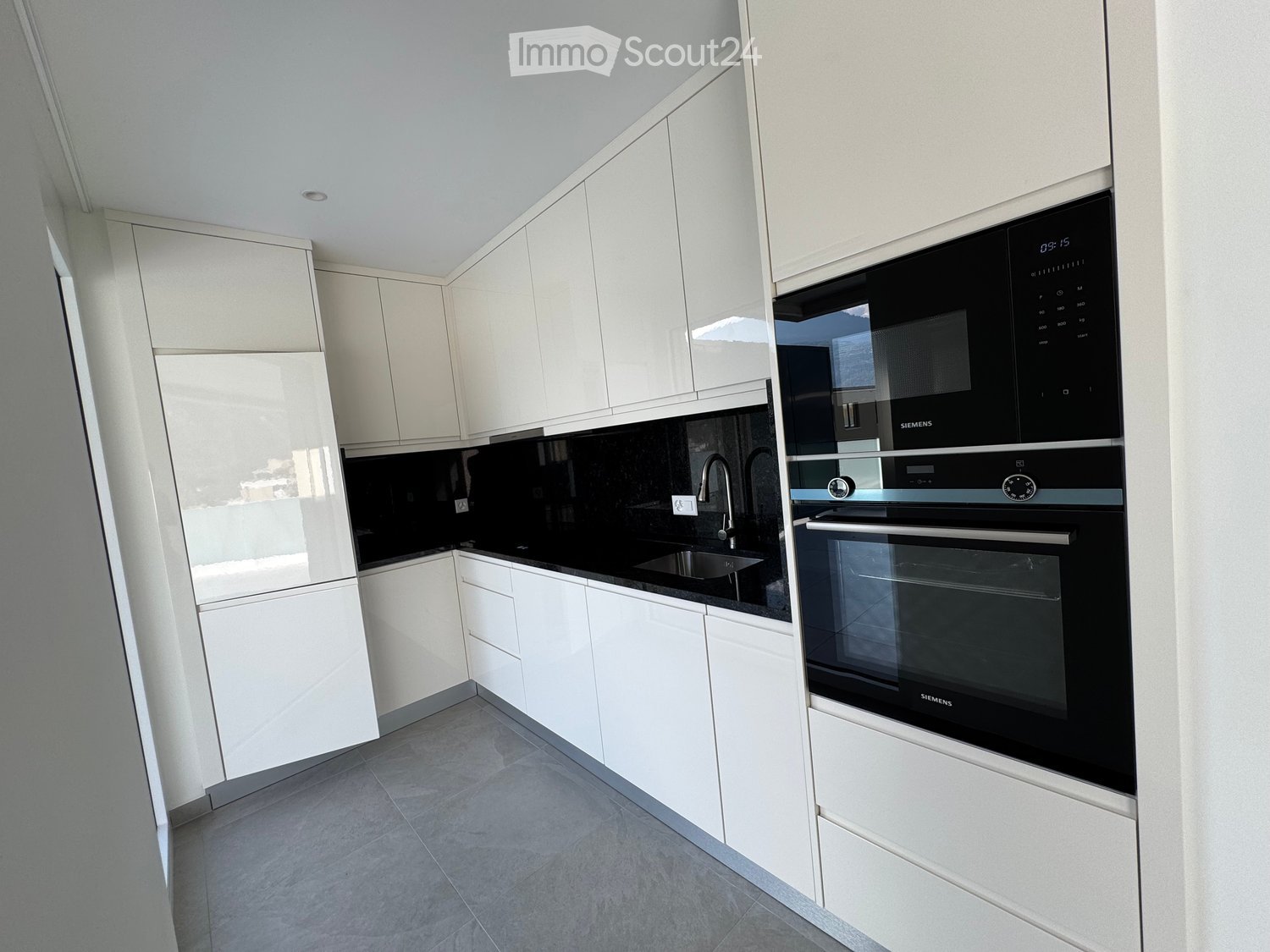 Modern kitchen with white cabinets, black countertop, stainless steel sink, and built-in Siemens oven and microwave.
