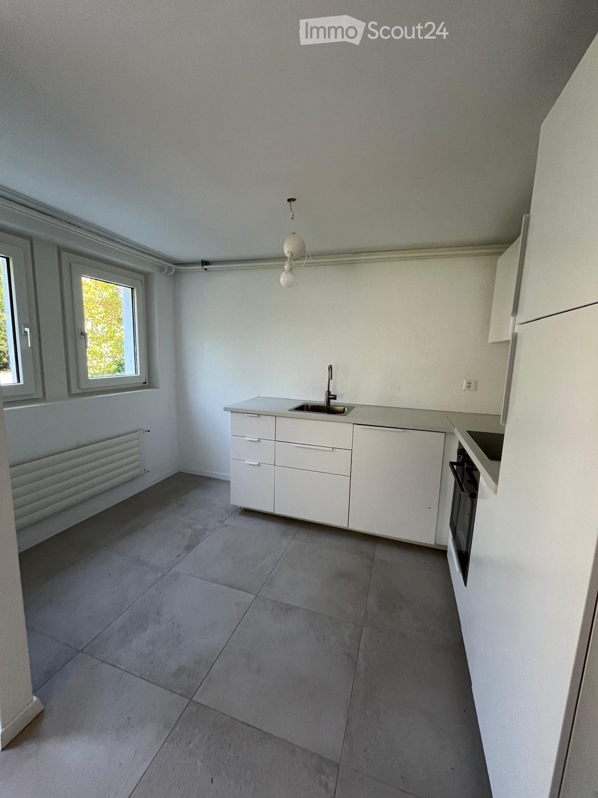 Modern kitchen with white cabinets, a sink, and an oven, featuring a tiled floor and large windows.