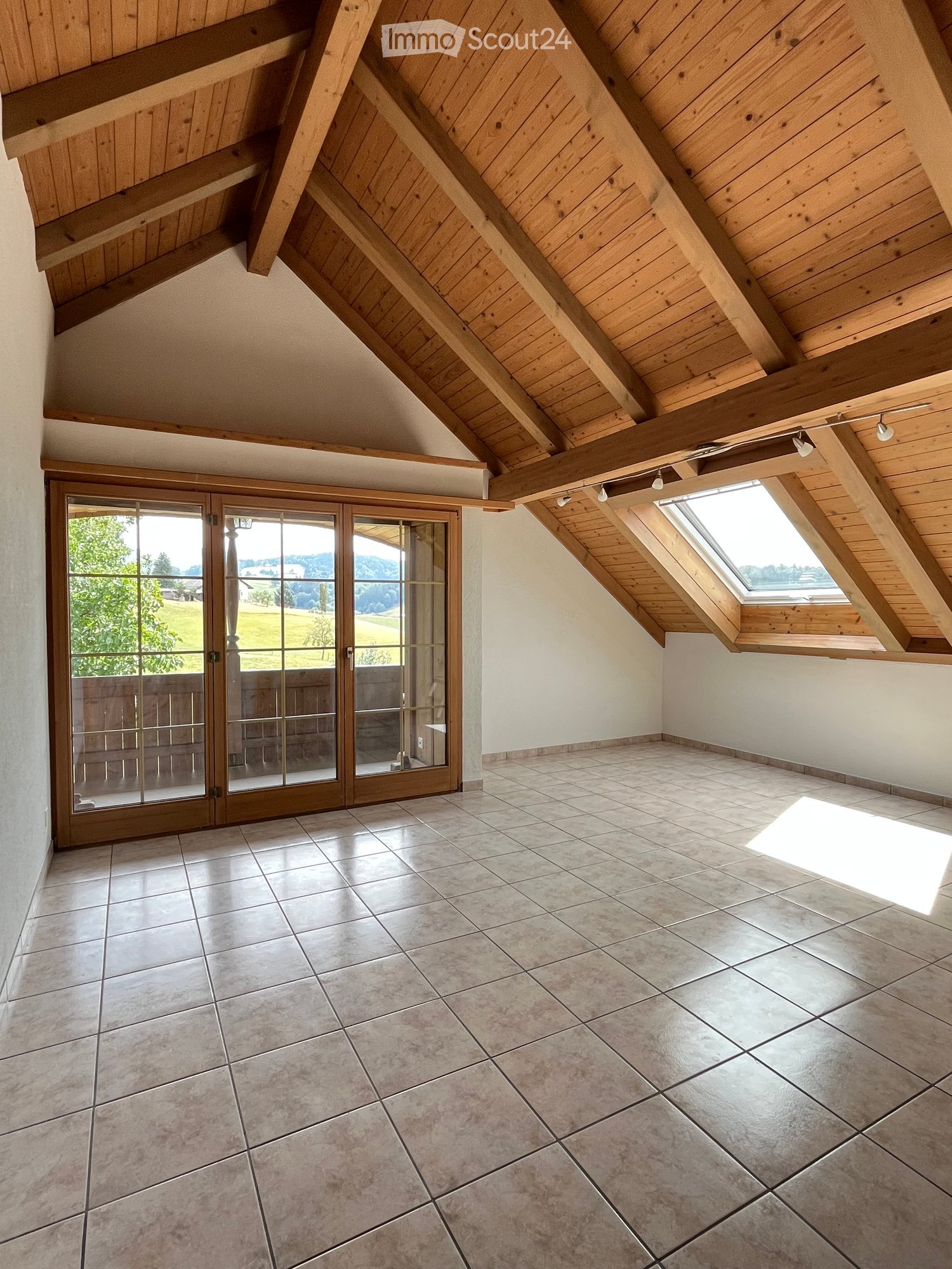 Empty room with exposed wooden beams on the ceiling, large skylight windows, and a sliding glass door leading to an outdoor area.