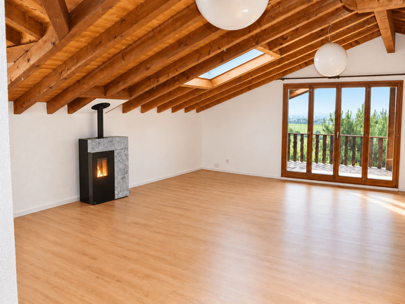 Bright, airy attic space with wooden beams, skylights, and a fireplace. Large sliding glass doors open to a balcony with scenic views.