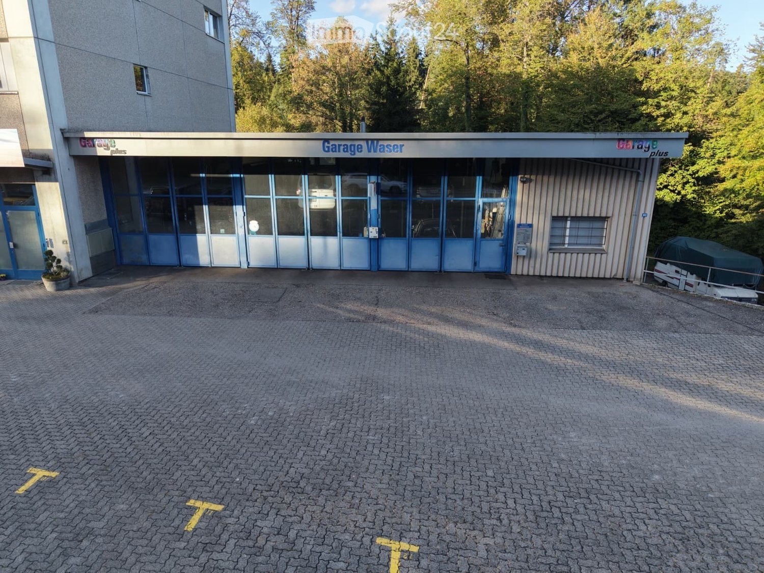 Garage entrance with multiple blue doors, adjacent building, and a paved driveway.