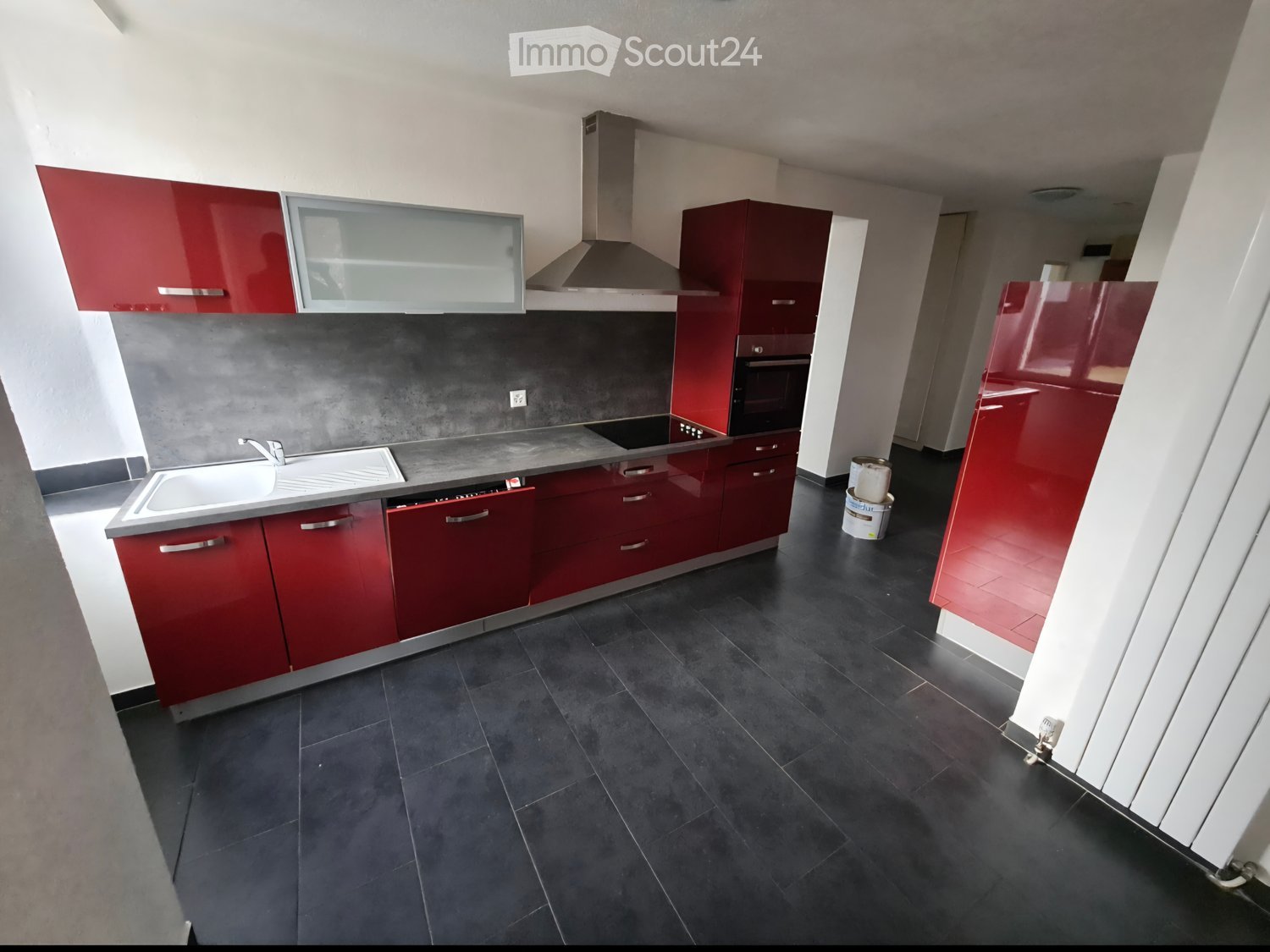 Modern kitchen with red cabinets, stainless steel appliances, and dark tiled flooring.