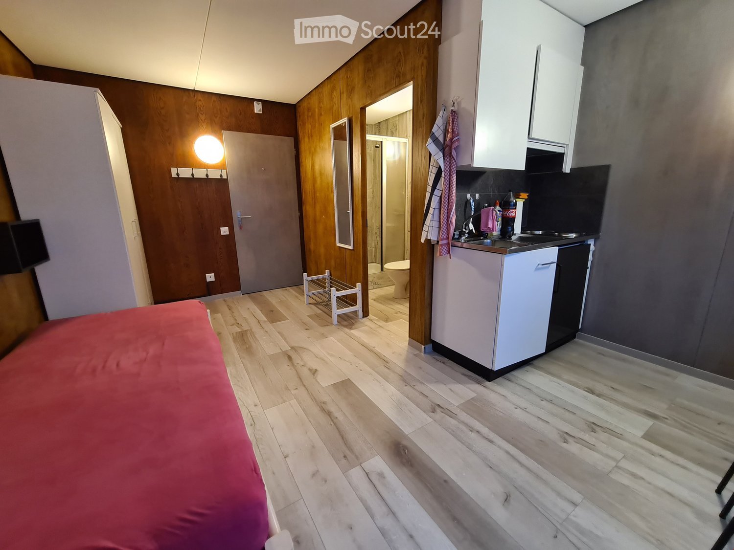 Compact room with a bed, small kitchenette, and a bathroom with toilet and shower. Wooden walls and floors.