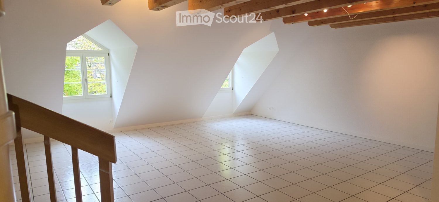 Empty attic room with white tiled floor, white walls, exposed wooden beams, and two skylight windows.