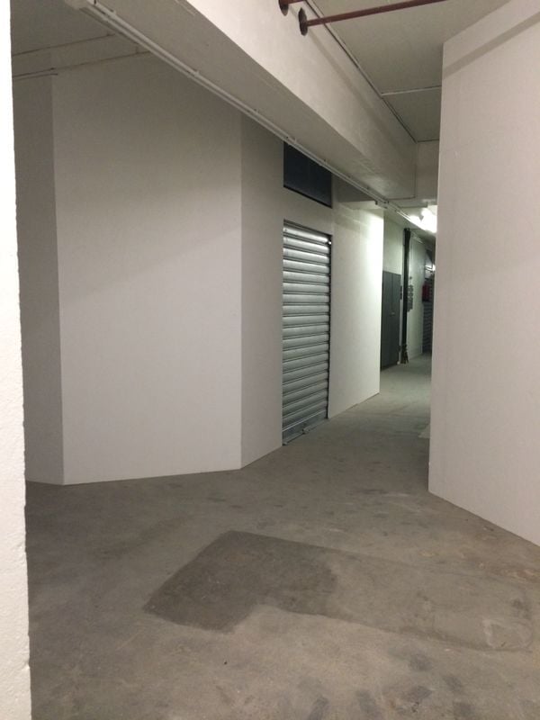 Empty parking lot with white walls, a concrete floor, and a single metal storage unit