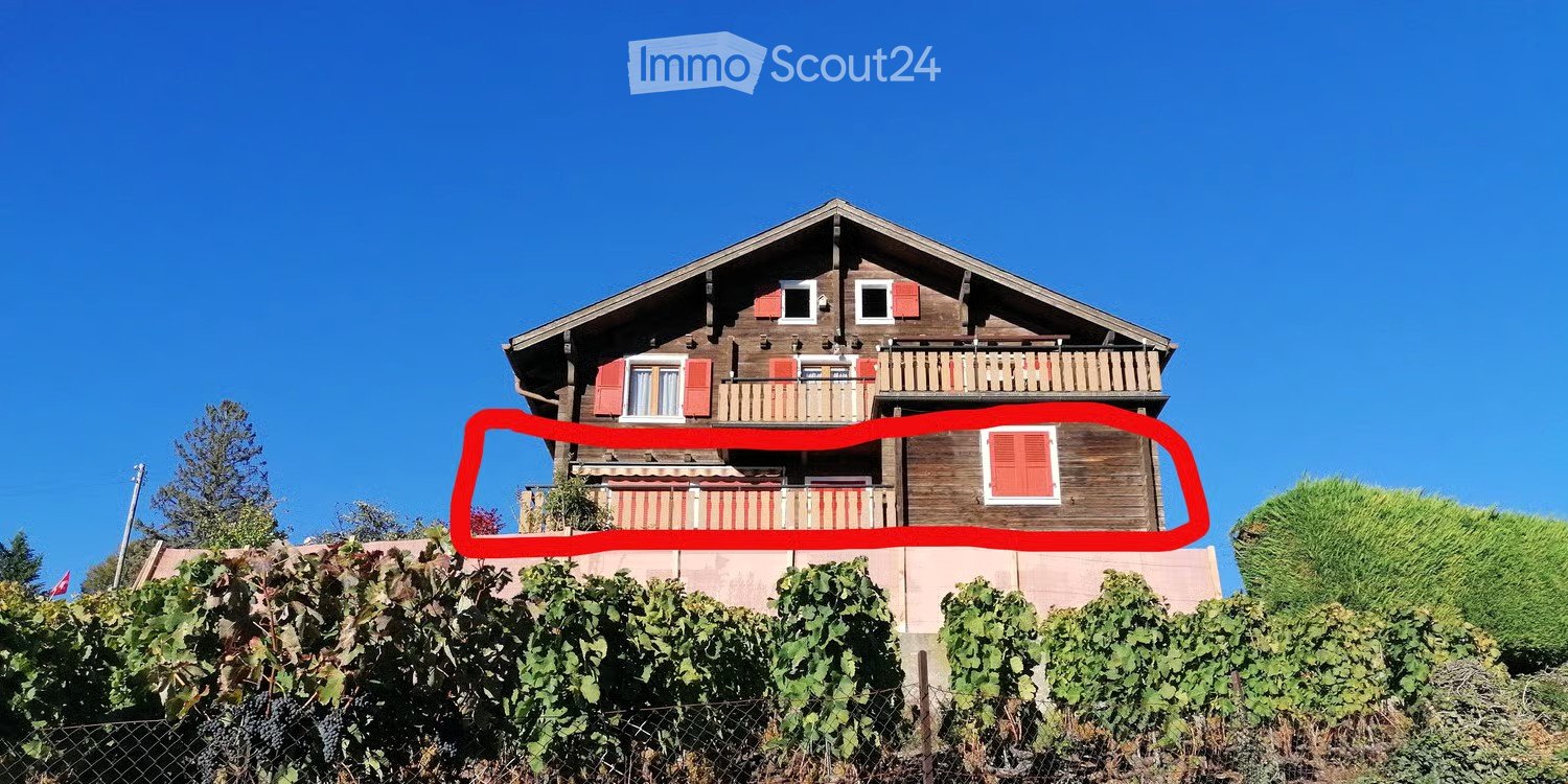 A two-story wooden house with red shutters, multiple windows, and balconies overlooking a vineyard.
