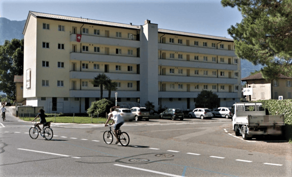 Multi-story building with multiple windows and balconies, located near a road with cyclists and parked cars.