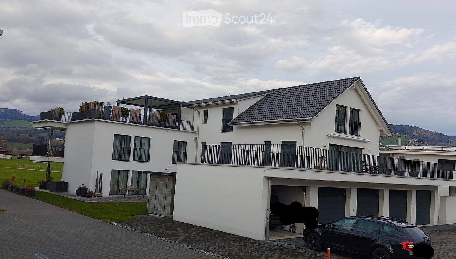 Modern two-story white house with multiple balconies, garage, and a parked car in front.