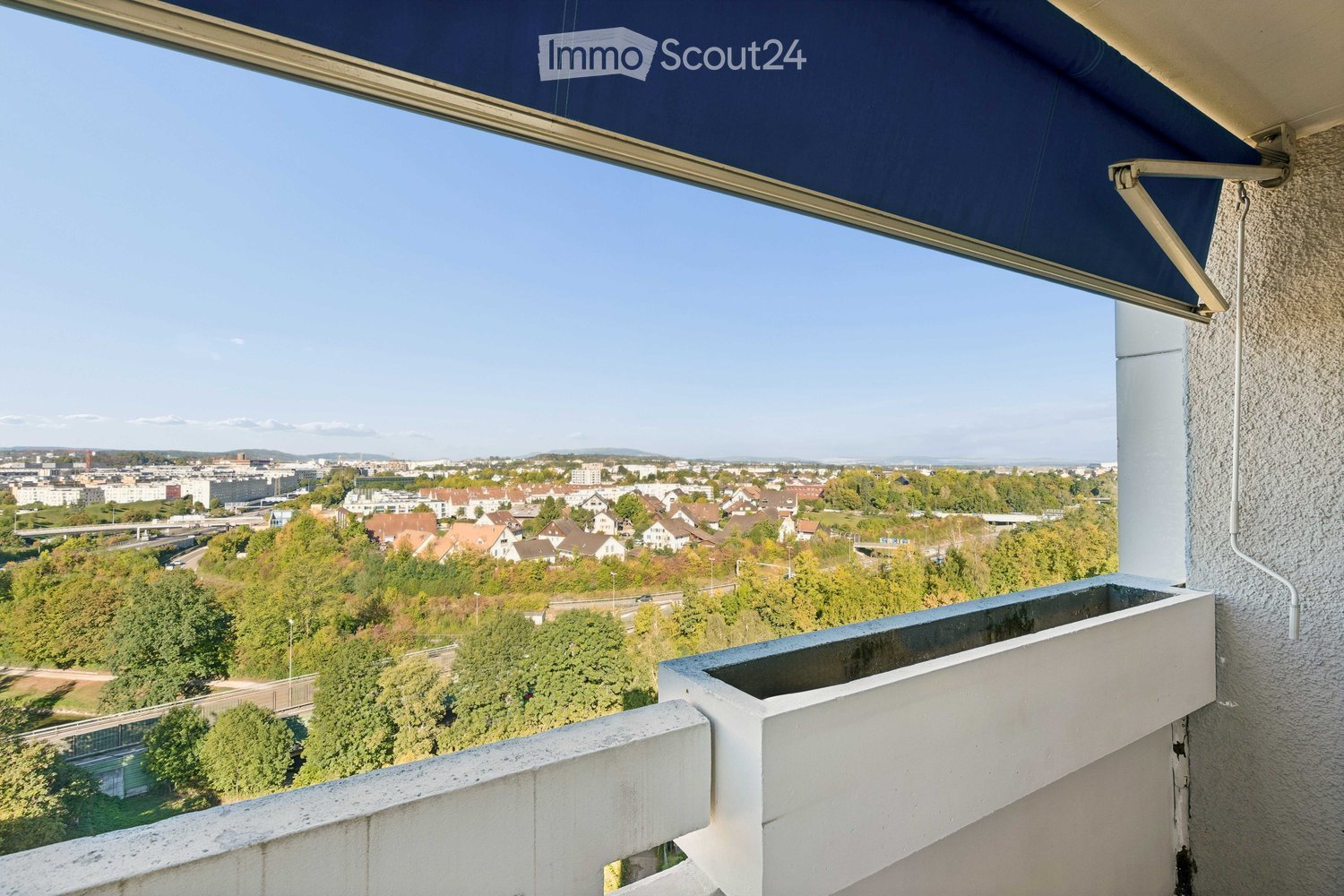 Balcony with a retractable awning, overlooking a cityscape with trees, buildings, and distant mountains.