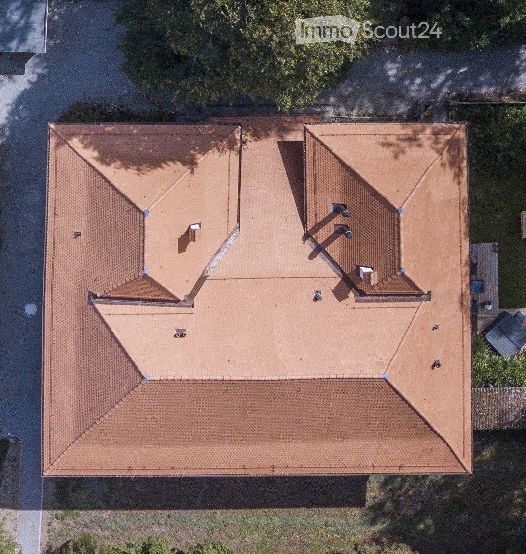 Aerial view of a house with a brown tiled roof, multiple chimneys, and surrounding greenery.