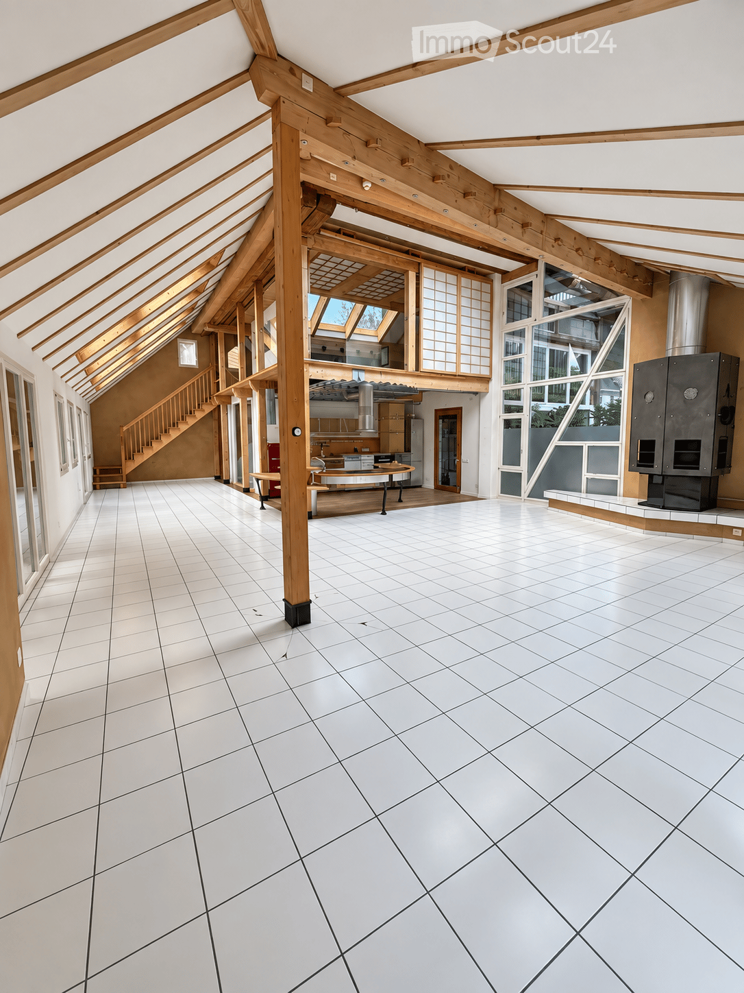 Bright, open room with white tiled flooring, wooden beams, and large windows. The space is empty, with no furniture or furnishings visible.