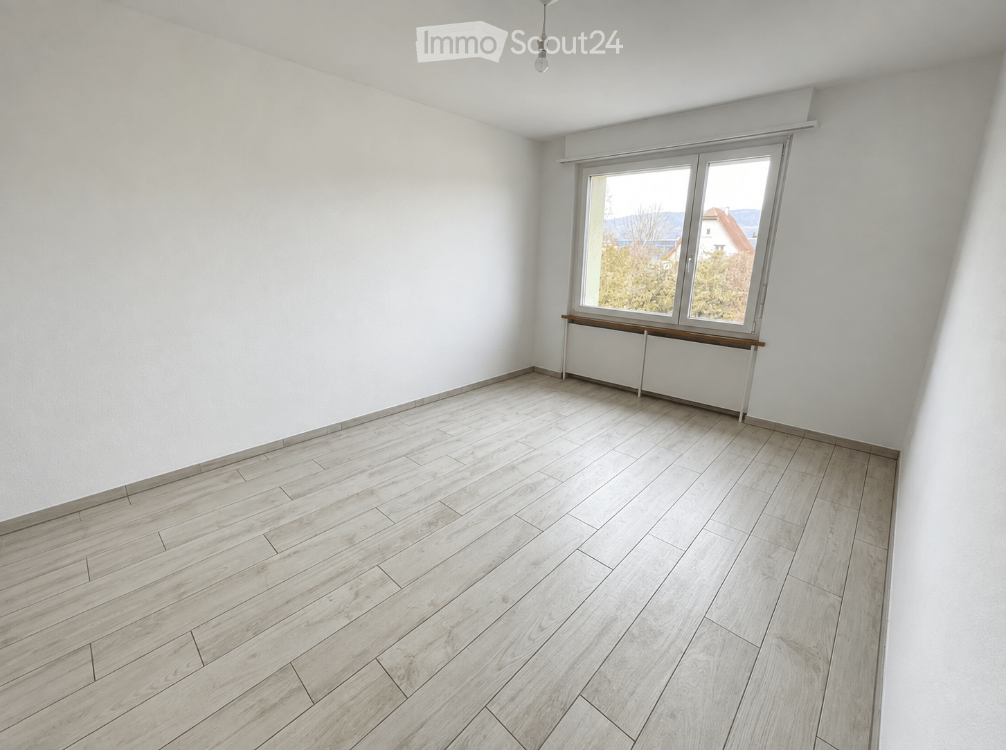 Empty room with light wooden flooring, white walls, and a large window with a simple wooden shelf below it.