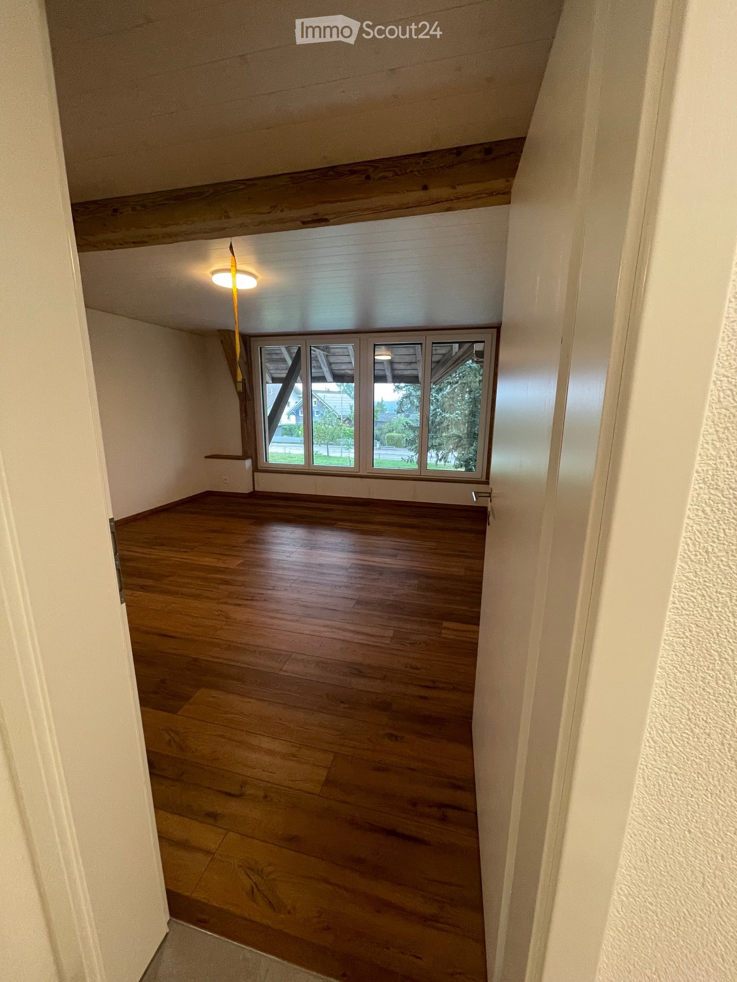 Empty room with wooden flooring, white walls, and large windows offering a view of the outdoors.