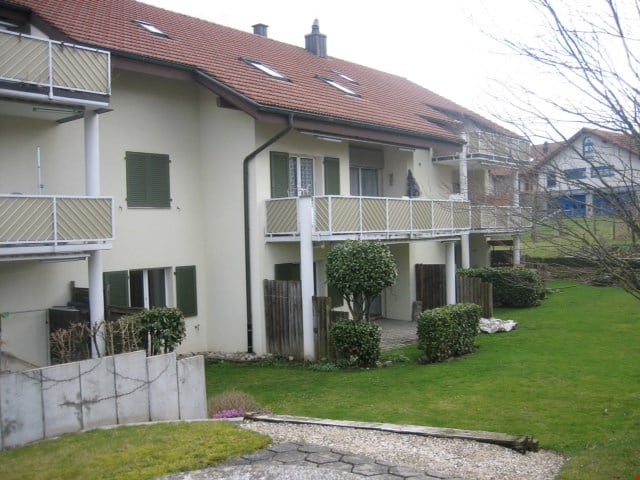 A multi-story residential building with balconies, green shutters, and a well-maintained lawn in front.
