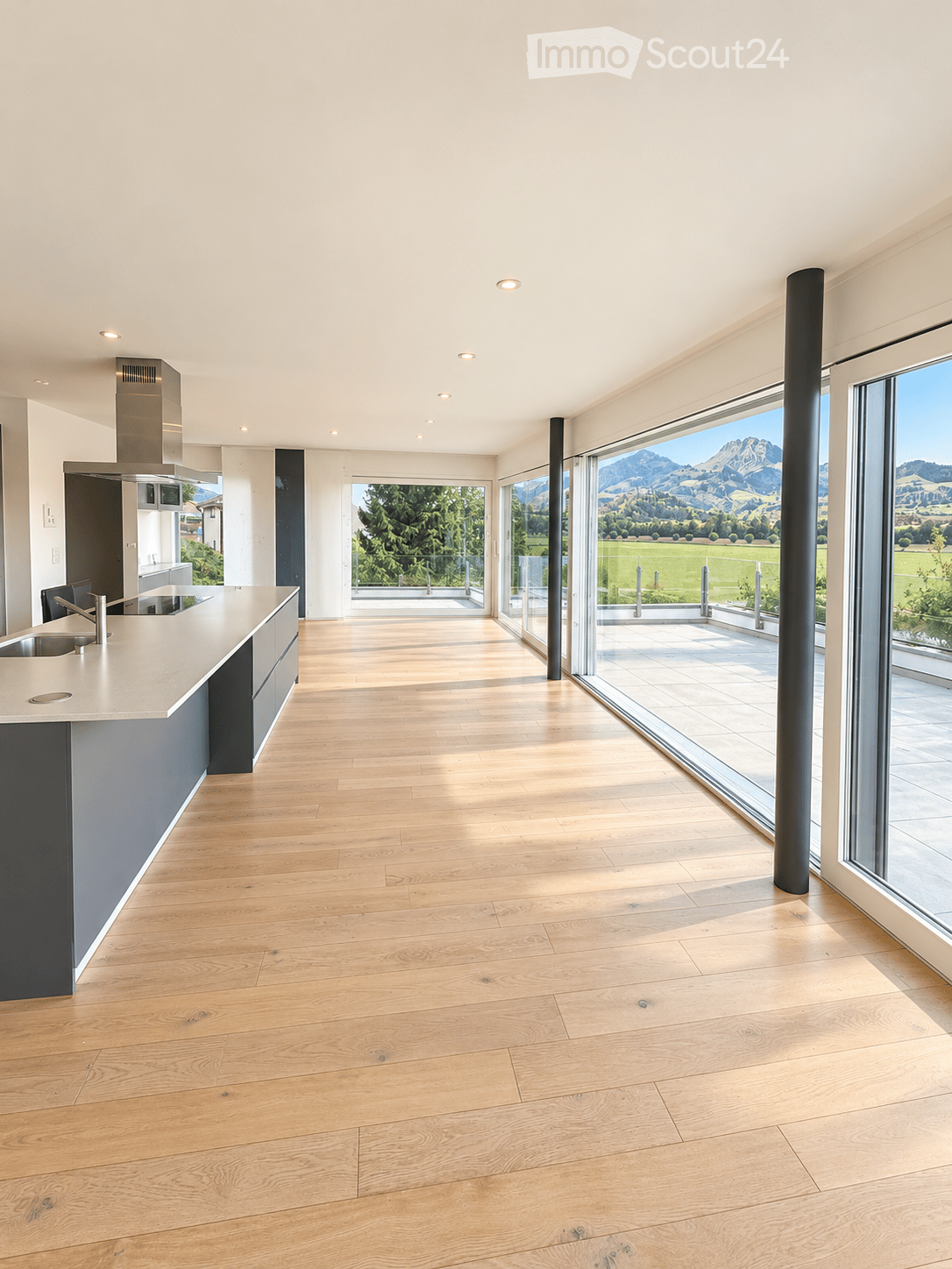 Modern kitchen with light wooden flooring, white cabinetry, and large windows offering a scenic mountain view.