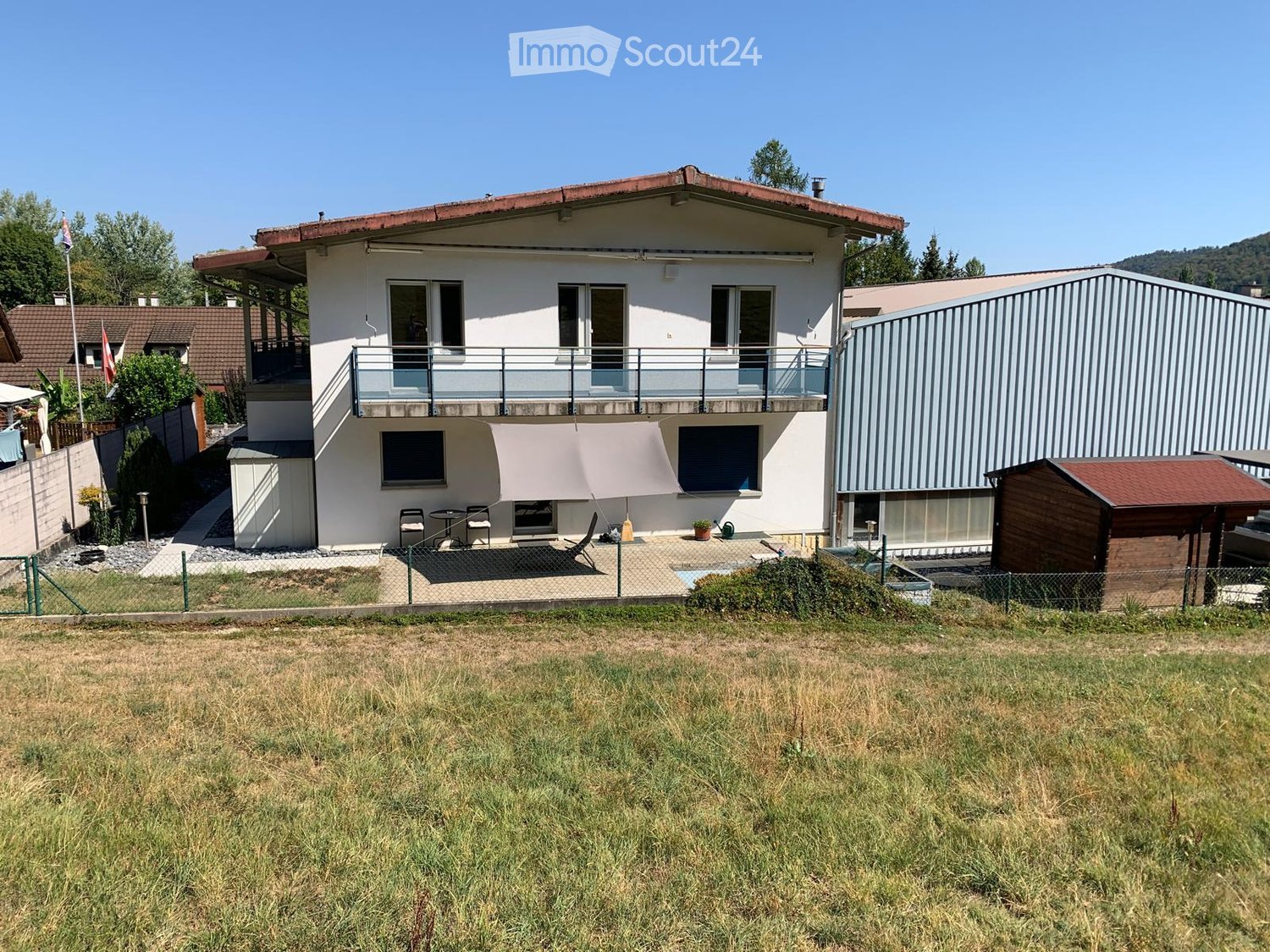 Two-story house with a balcony, patio, and surrounding garden area.