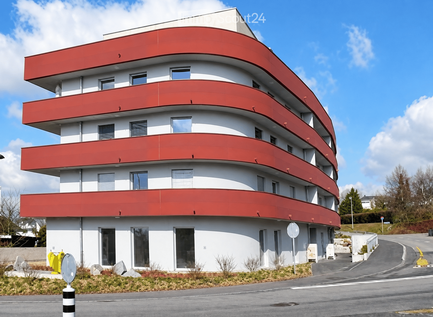 Modern, multi-story building with white walls and red accents, featuring large windows and balconies.
