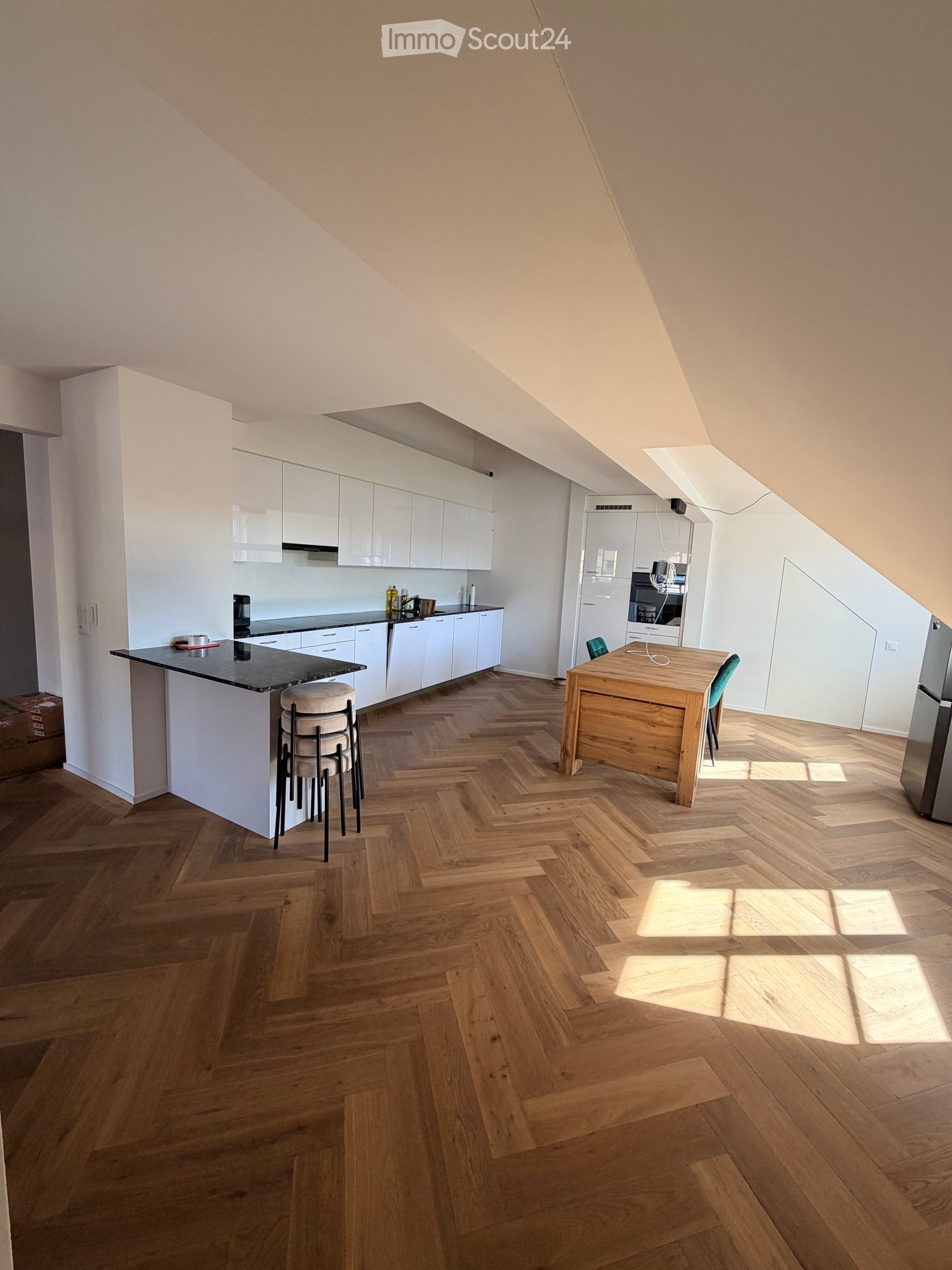 Modern kitchen with white cabinets, a black countertop kitchen island, a wooden dining table, and a herringbone wooden floor.