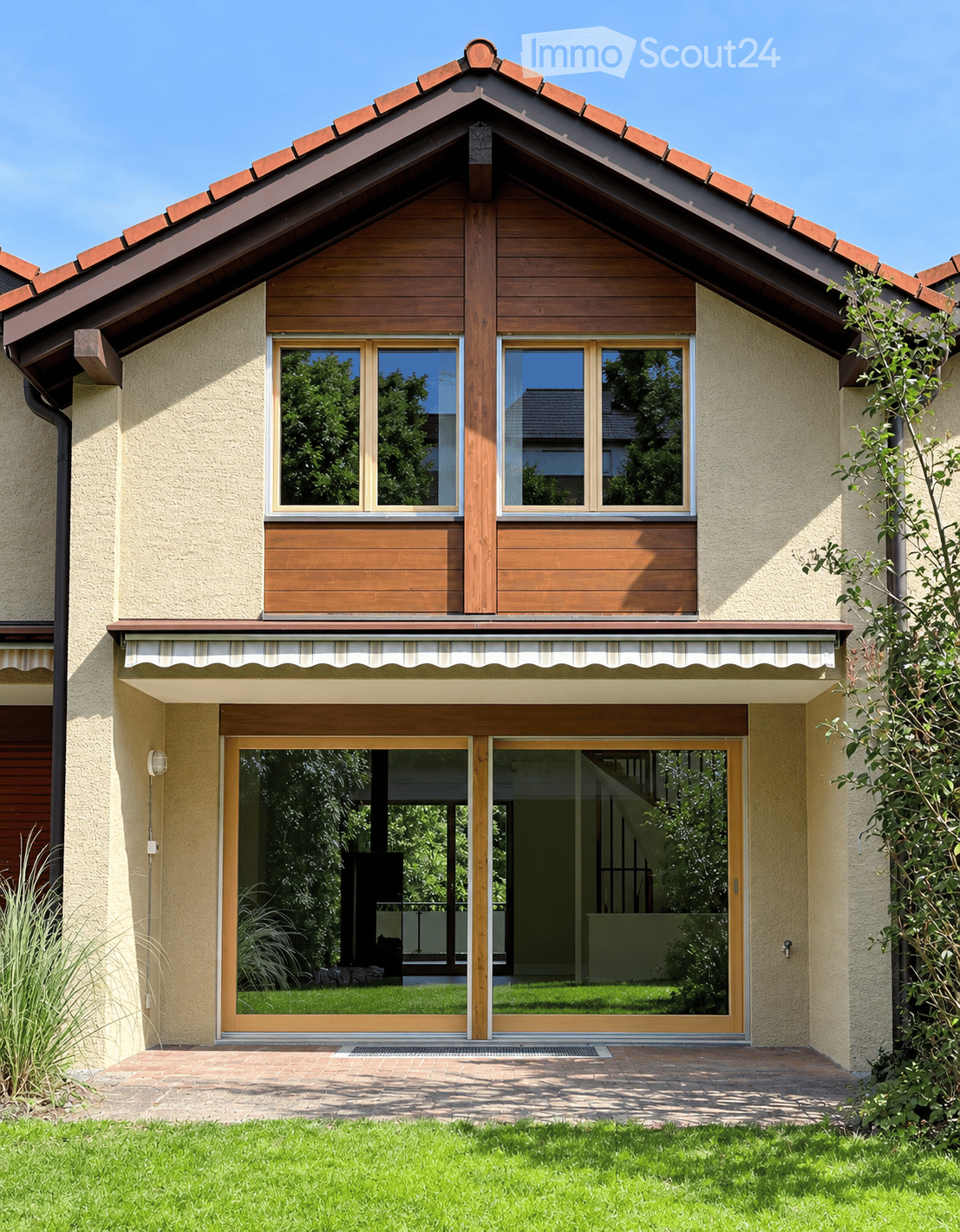 Two-story house with a red-tiled roof, wooden accents, large windows, and a covered entrance with sliding glass doors.