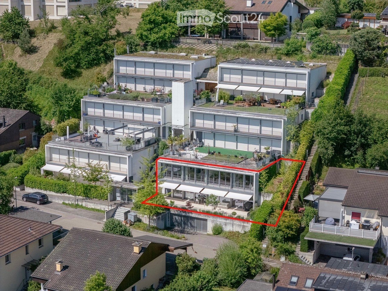 Aerial view of a modern, multi-story residential complex with large glass windows, terraces, and surrounding greenery.