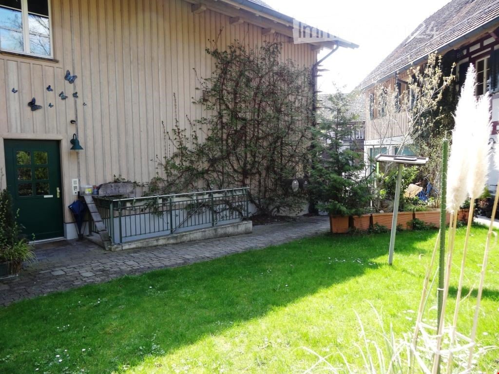 Garden area with green grass, small pathway, wooden house with green door, climbing plants, and decorative elements.