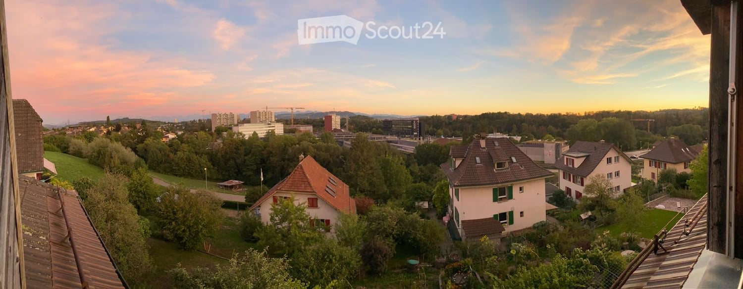 Balcony view overlooking a suburban neighborhood with houses, trees, and distant cityscape at sunset.