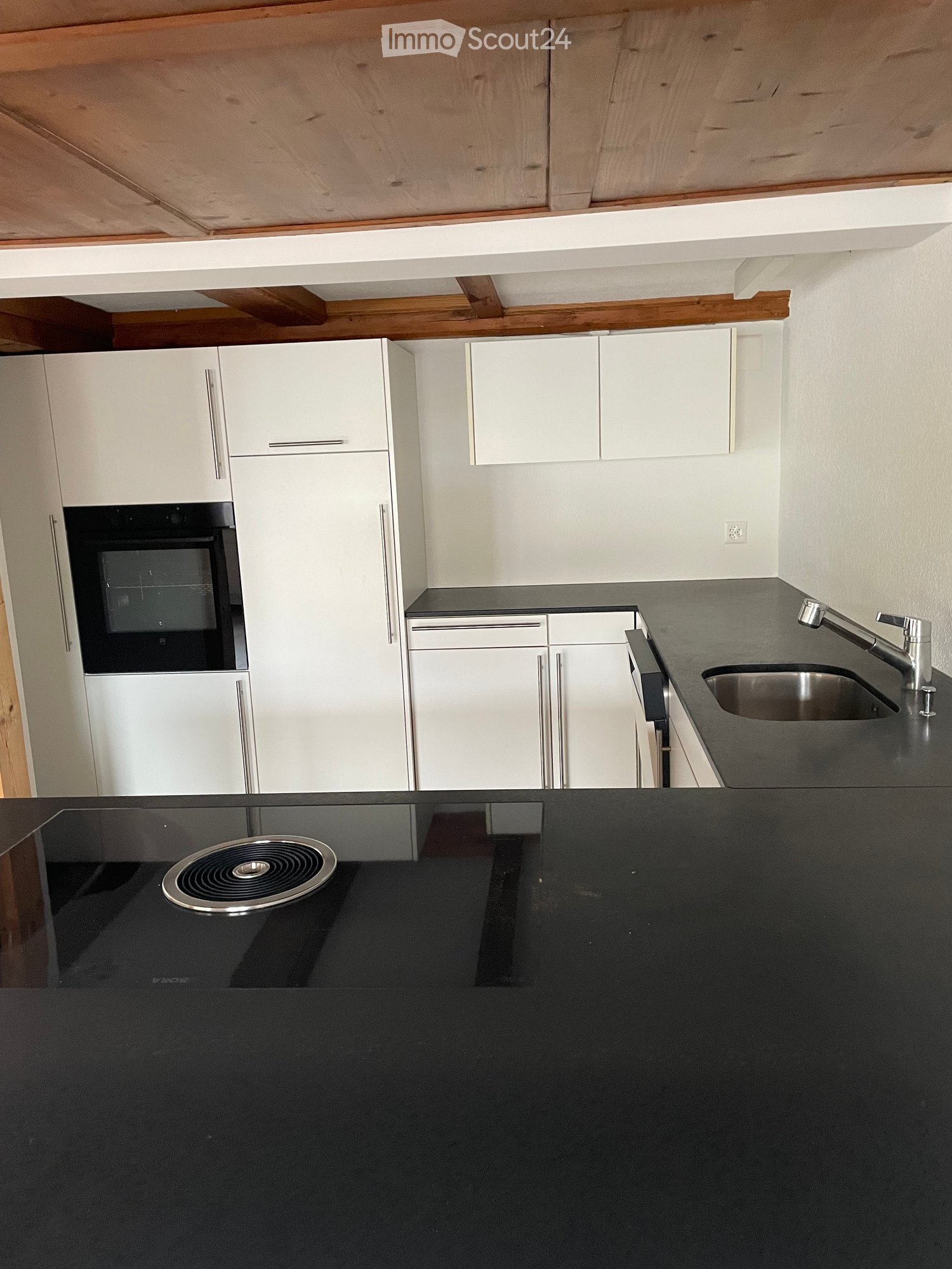 Modern kitchen with white cabinets, black countertops, stainless steel sink, and built-in oven.