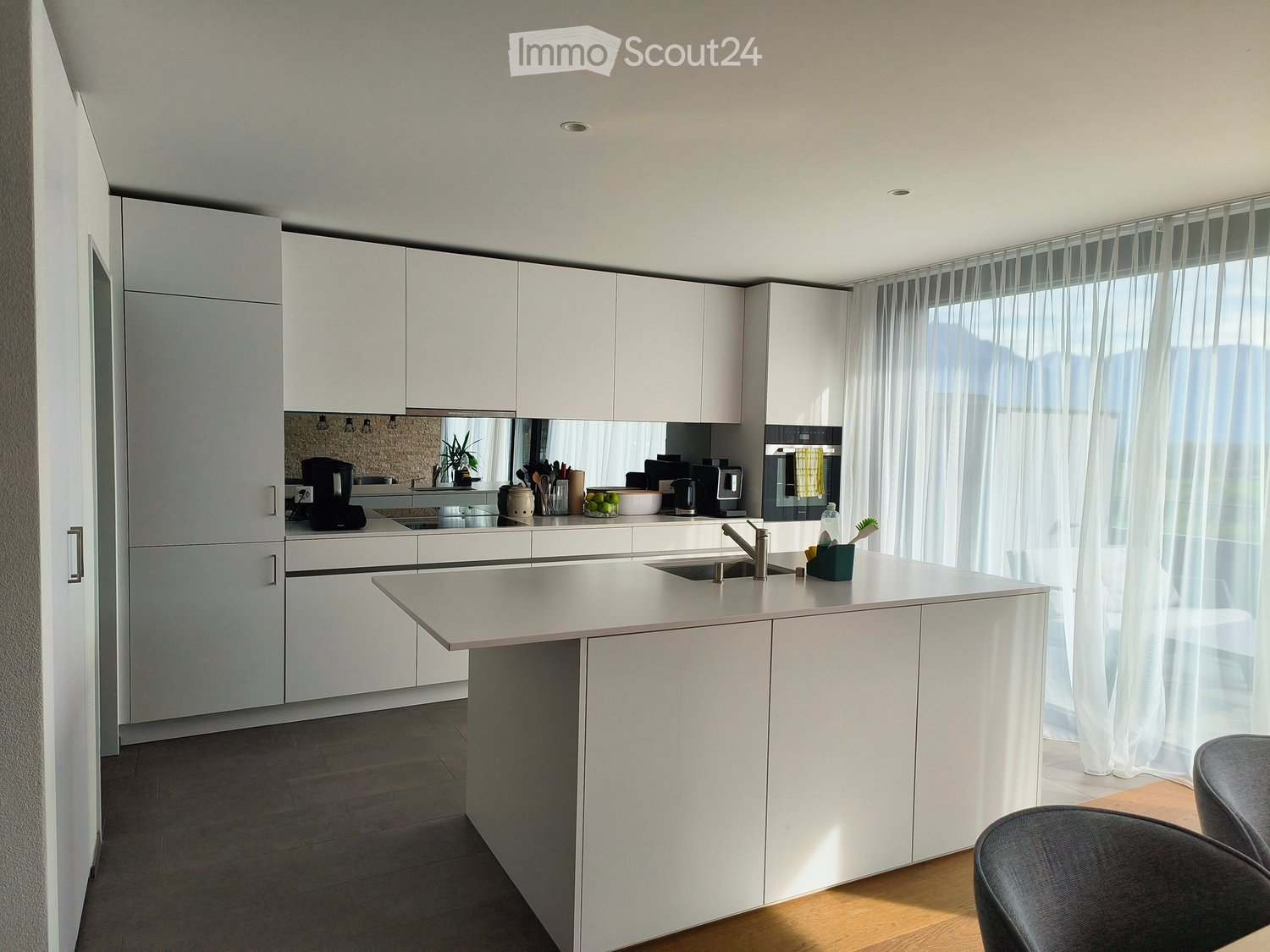 Modern kitchen with white cabinets, a central island, and a sink. Appliances and small items are visible on the counter.