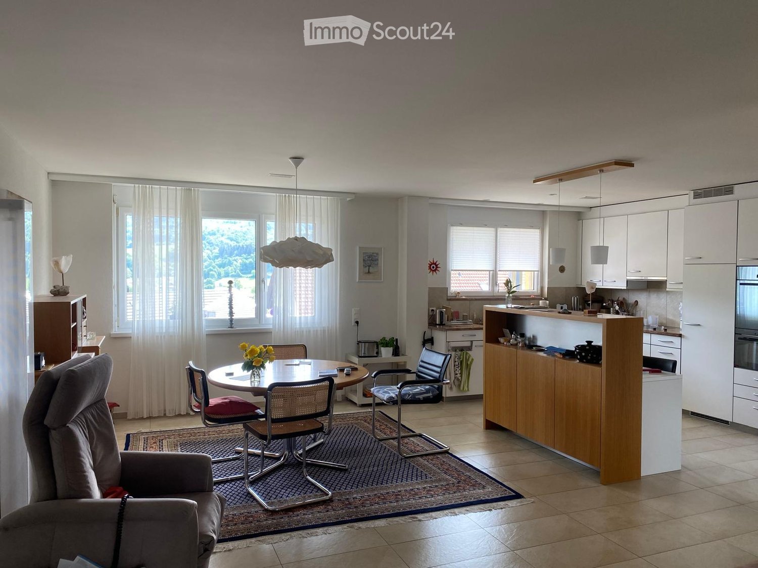 Open-plan living and dining area with a sofa, dining table, chairs, and a modern kitchen featuring white cabinets, a counter, and appliances.
