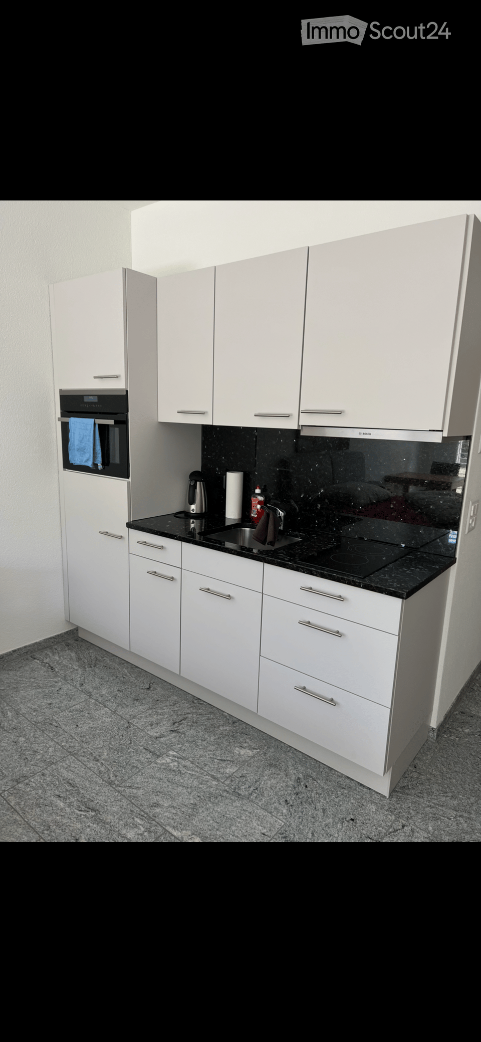 Modern kitchen with white cabinets, black granite countertops, and stainless steel appliances including an oven, sink, and electric kettle.
