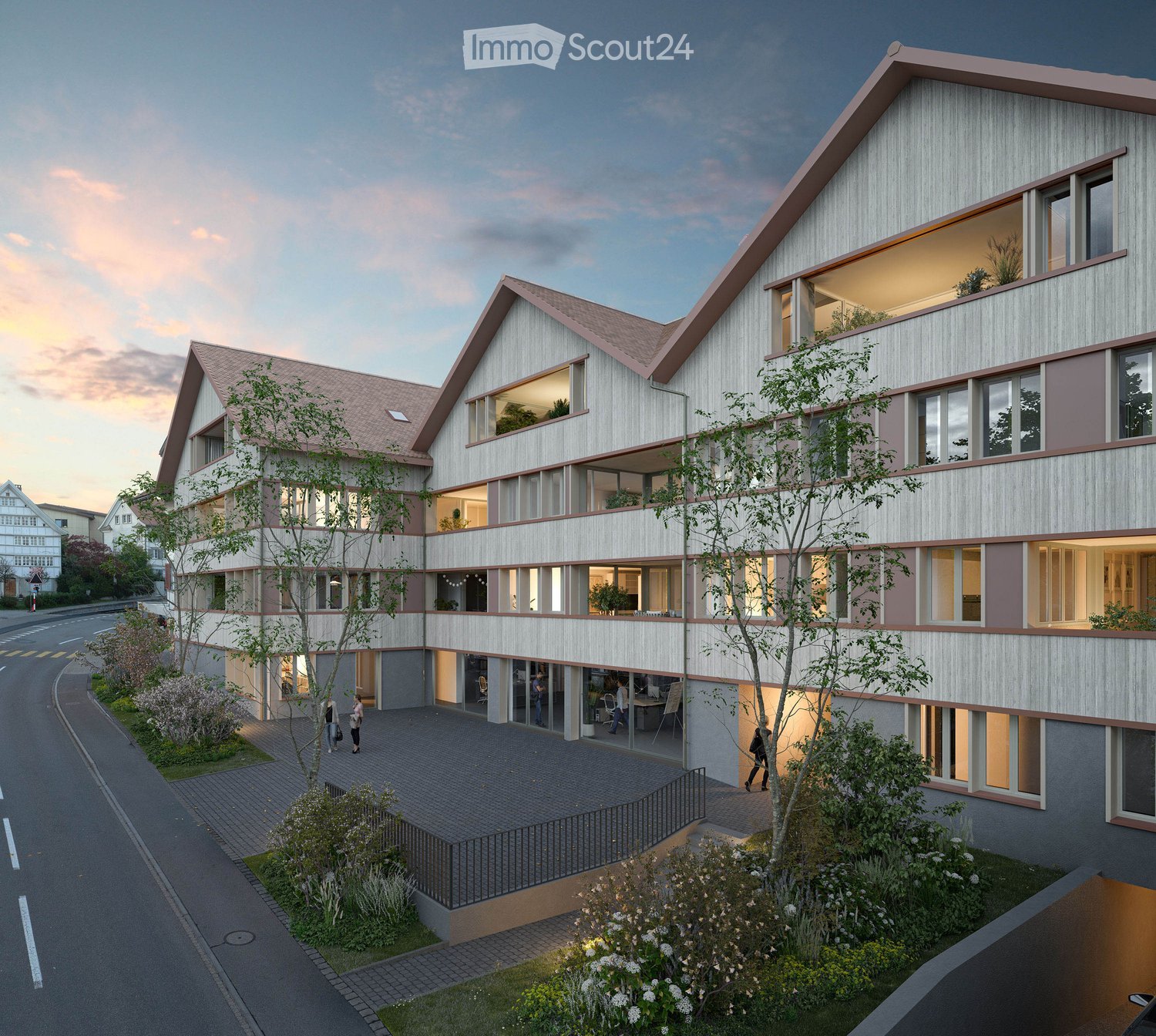 Modern multi-story residential building with a contemporary design, featuring large windows, a sloped roof, and a raised ground floor. The building is surrounded by greenery and has a paved entrance area.