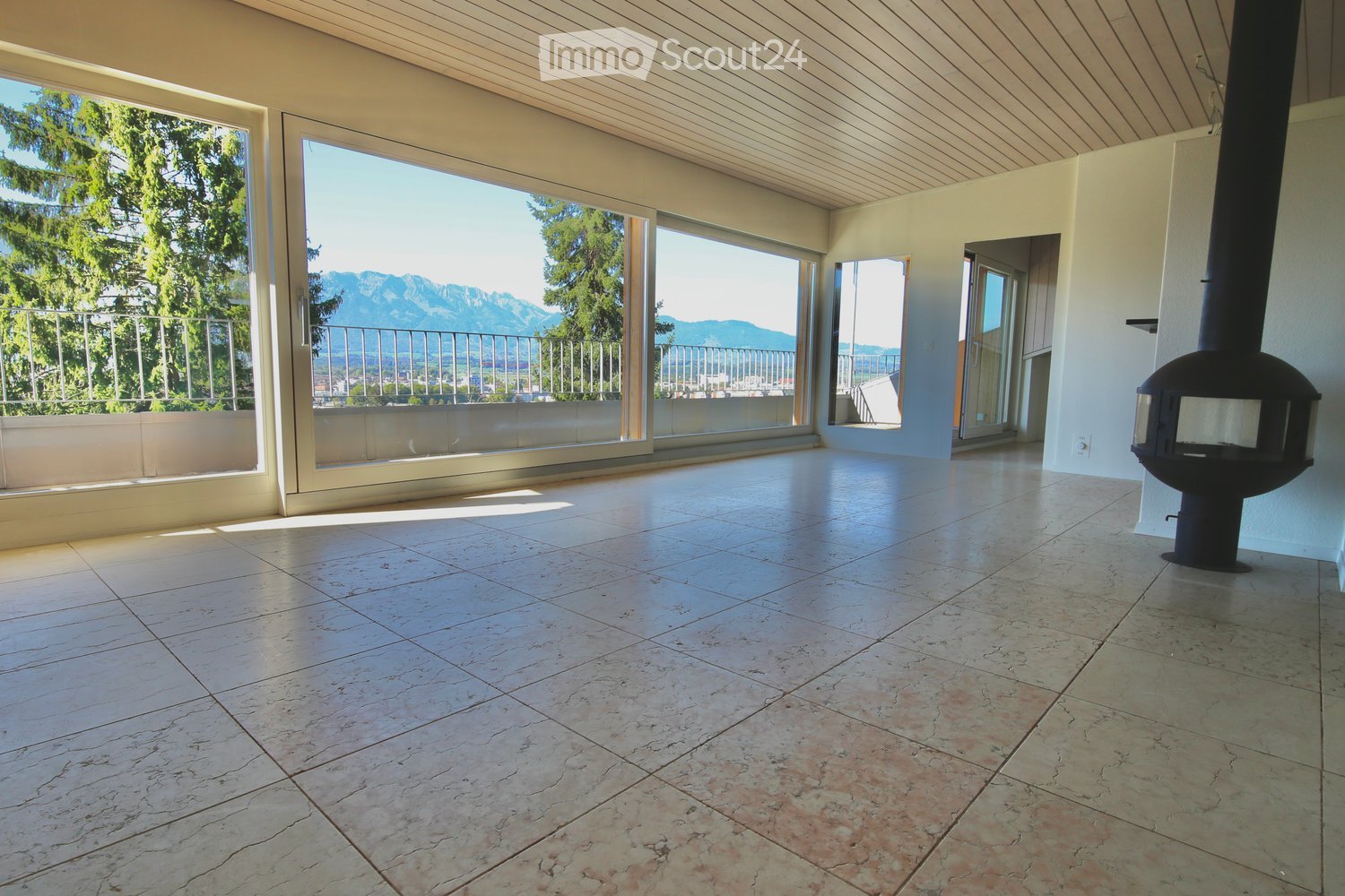Empty room with large windows and a view of mountains, featuring a tiled floor and a fireplace insert.