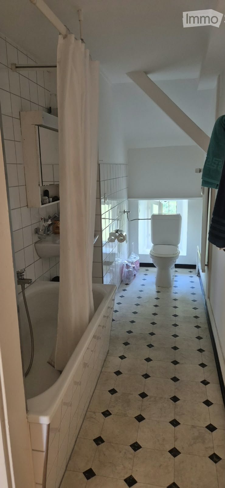 Bathroom with a bathtub, toilet, sink, and shower curtain. The floor has a patterned tile design, and there is a small window providing natural light.