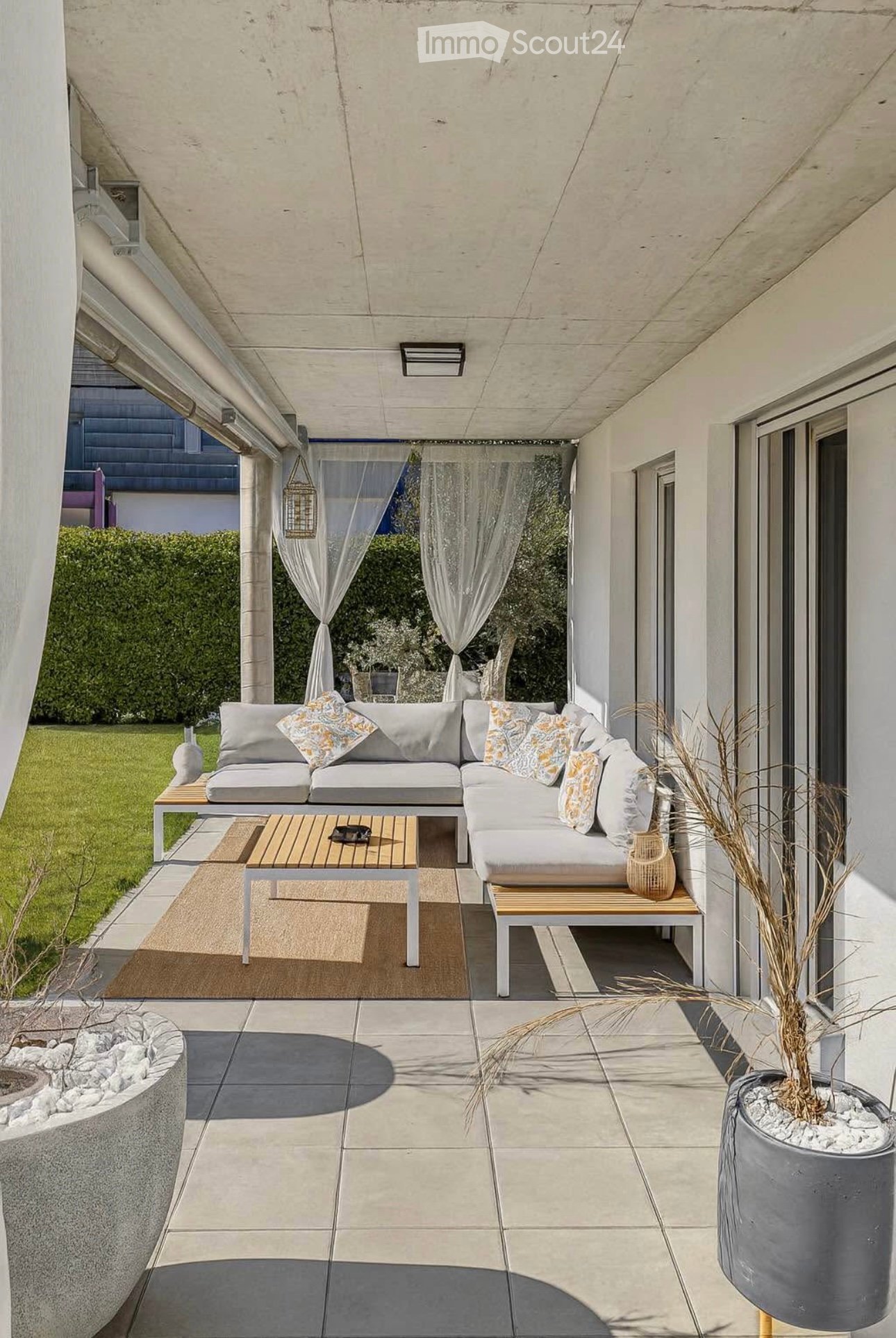 Modern outdoor patio with a grey sectional sofa, wooden coffee table, and decorative vases.