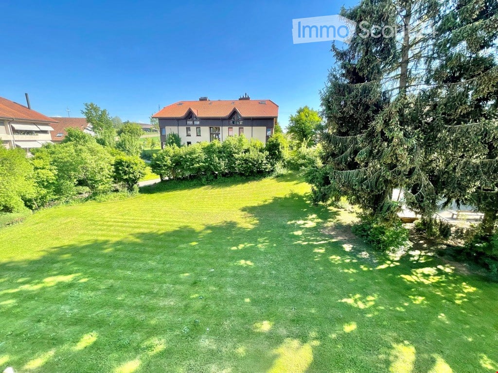 A well-maintained lawn with trees and bushes, leading to a two-story house with a red-tiled roof and white walls.