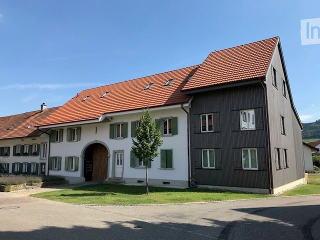 A two-story building with a red-tiled roof, white and dark brown facade, multiple windows, and a central arched entrance.