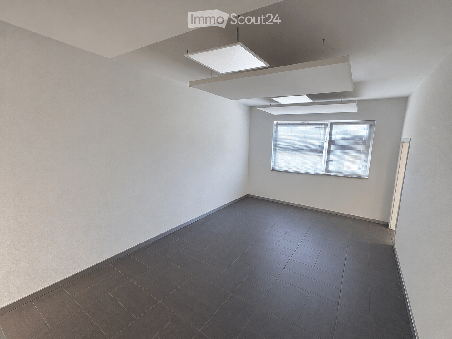 Empty room with white walls, dark tiled floor, large window with blinds, and modern ceiling lights.