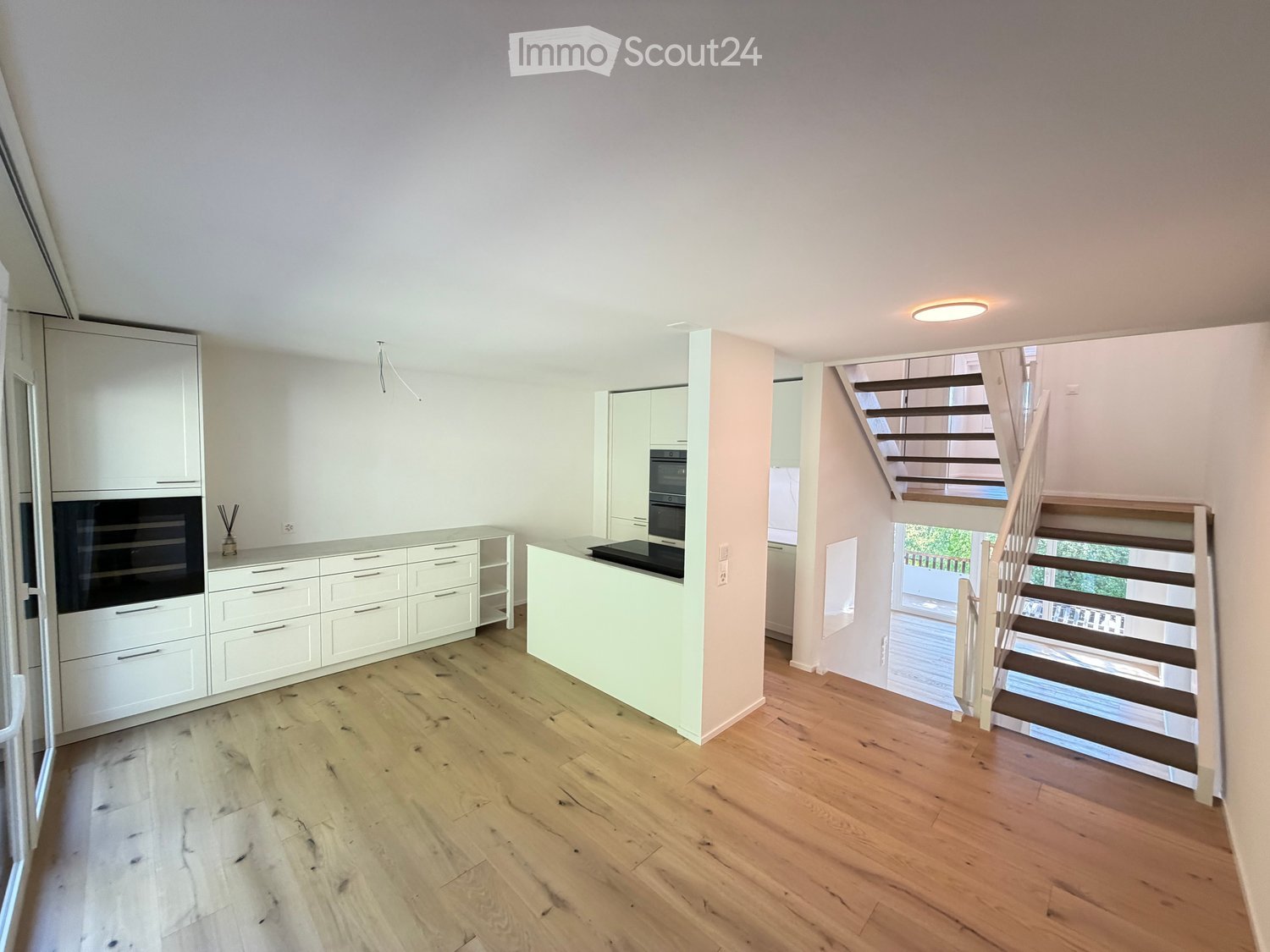 Modern kitchen with white cabinets, wooden flooring, and a staircase leading to another level.