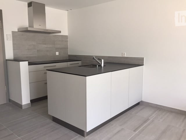 Modern kitchen with white cabinets, a central island, and a stainless steel range hood. The island features a black countertop with a sink and faucet.