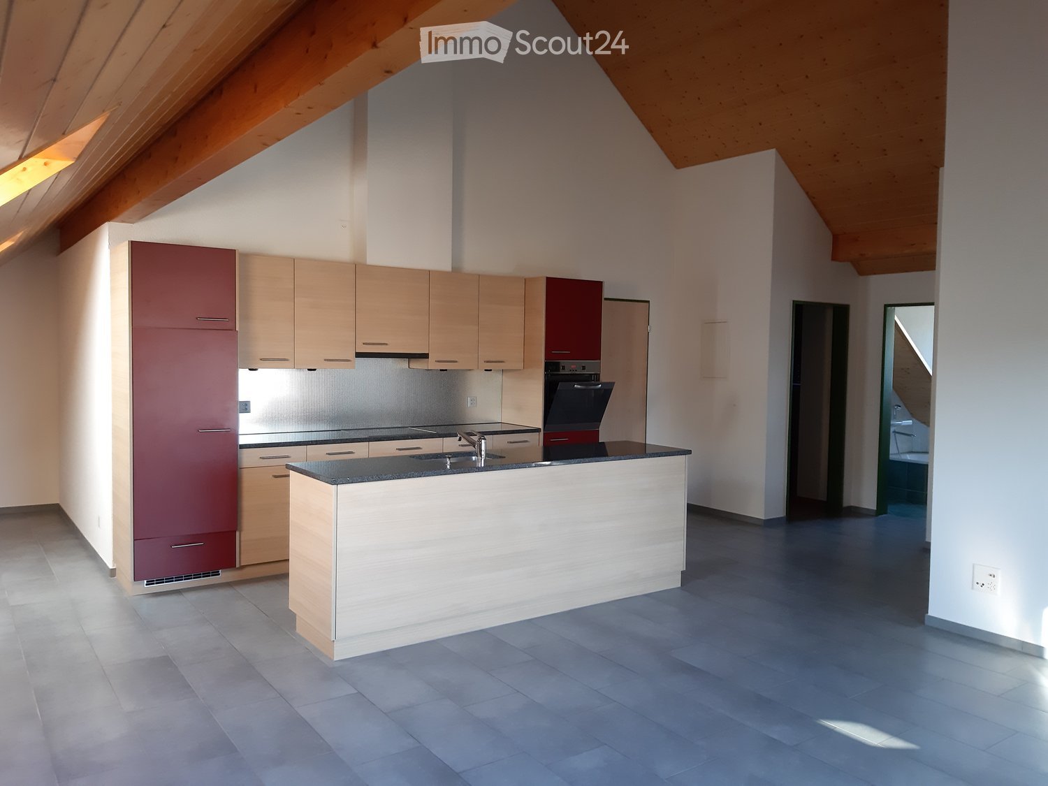 Modern kitchen with light wood cabinets, stainless steel appliances, and a central island with a black countertop.