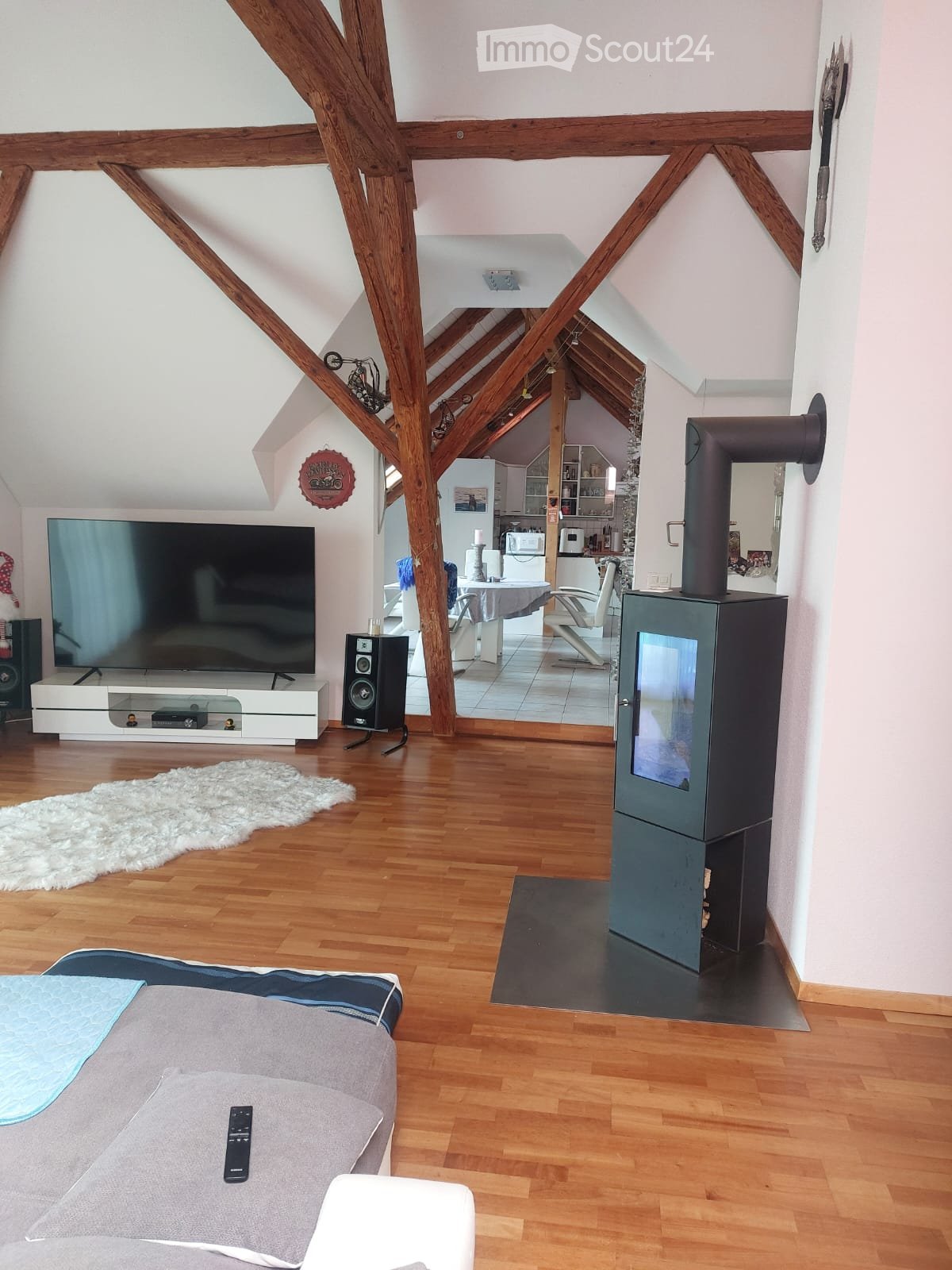 Spacious living area with exposed wooden beams, fireplace, television, sofa, coffee table, and an open kitchen area with appliances.