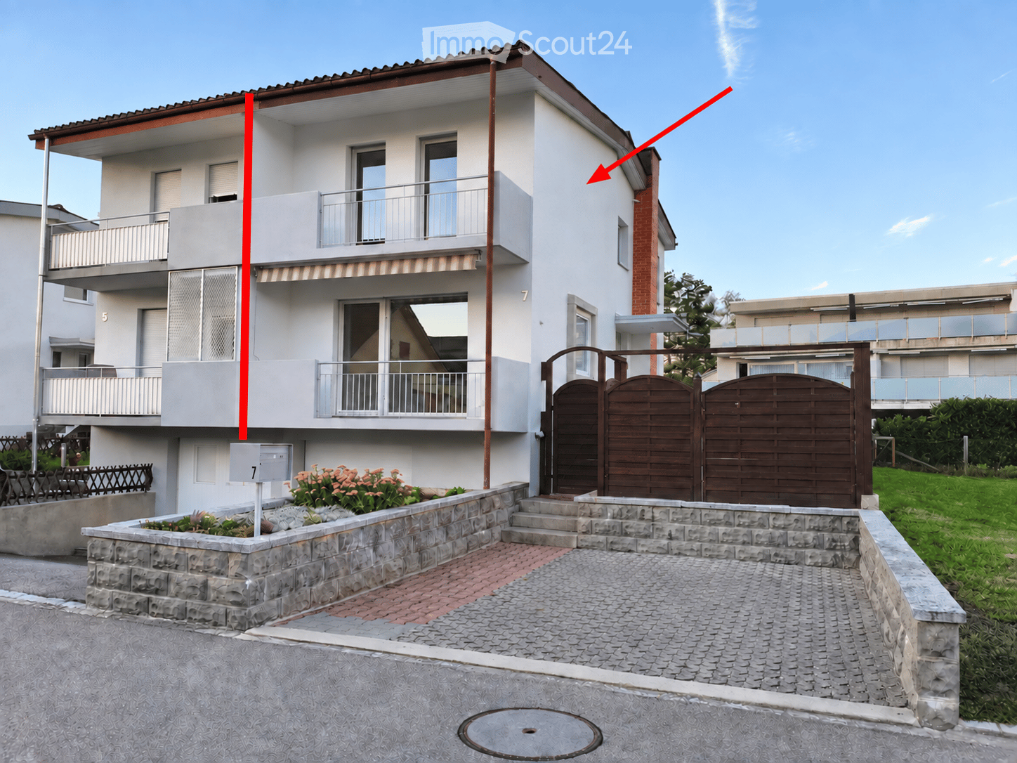 Two-story house with white exterior, multiple windows, balconies, and a gated driveway.