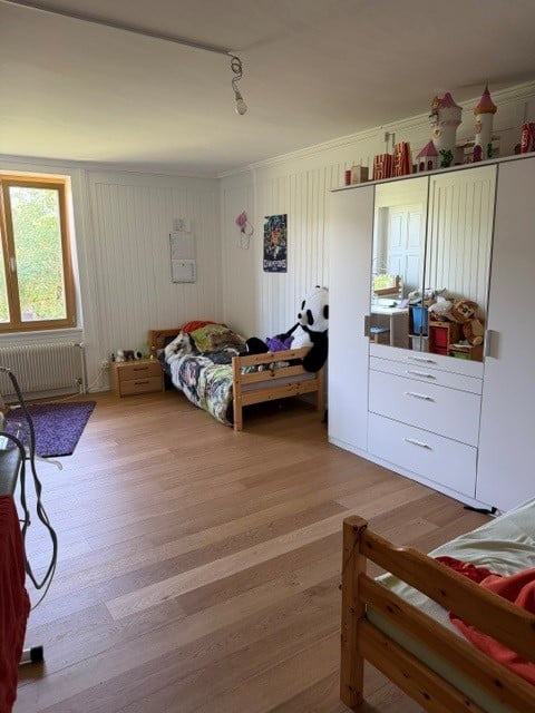 Cozy children's bedroom with wooden flooring, a single bed with colorful bedding, a large white wardrobe with mirrored doors, a nightstand, and various toys and decorations.