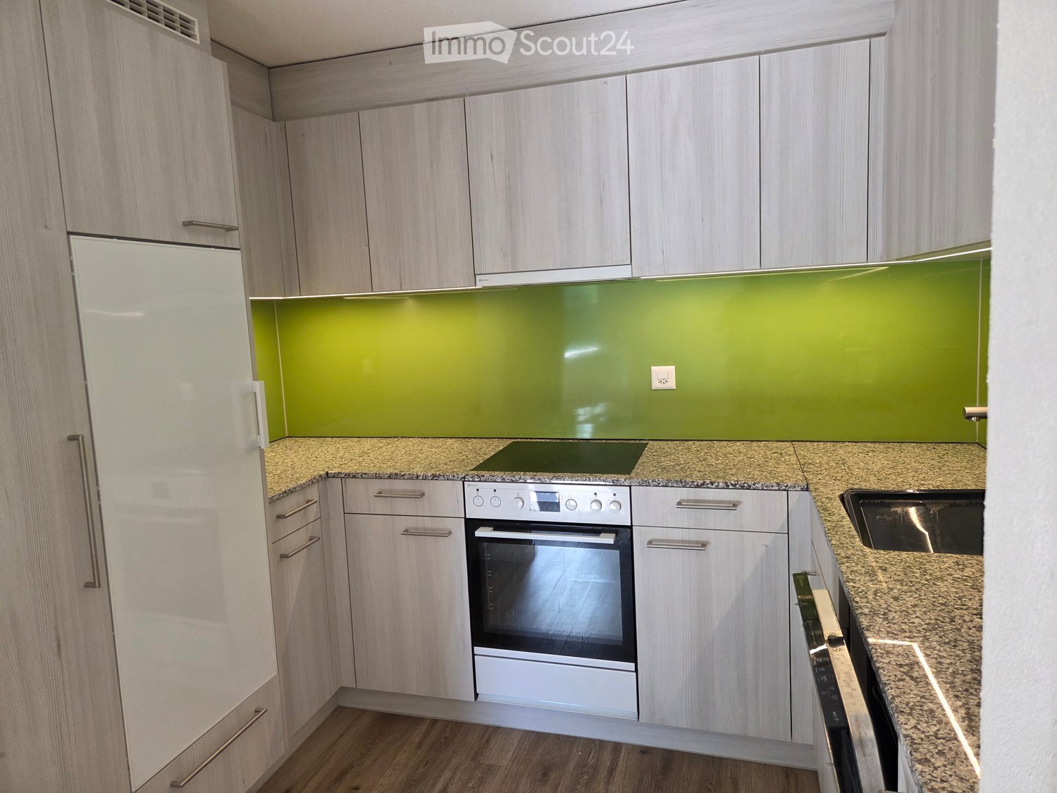 Modern kitchen with light wood cabinets, granite countertops, and stainless steel appliances including a refrigerator, oven, and sink.
