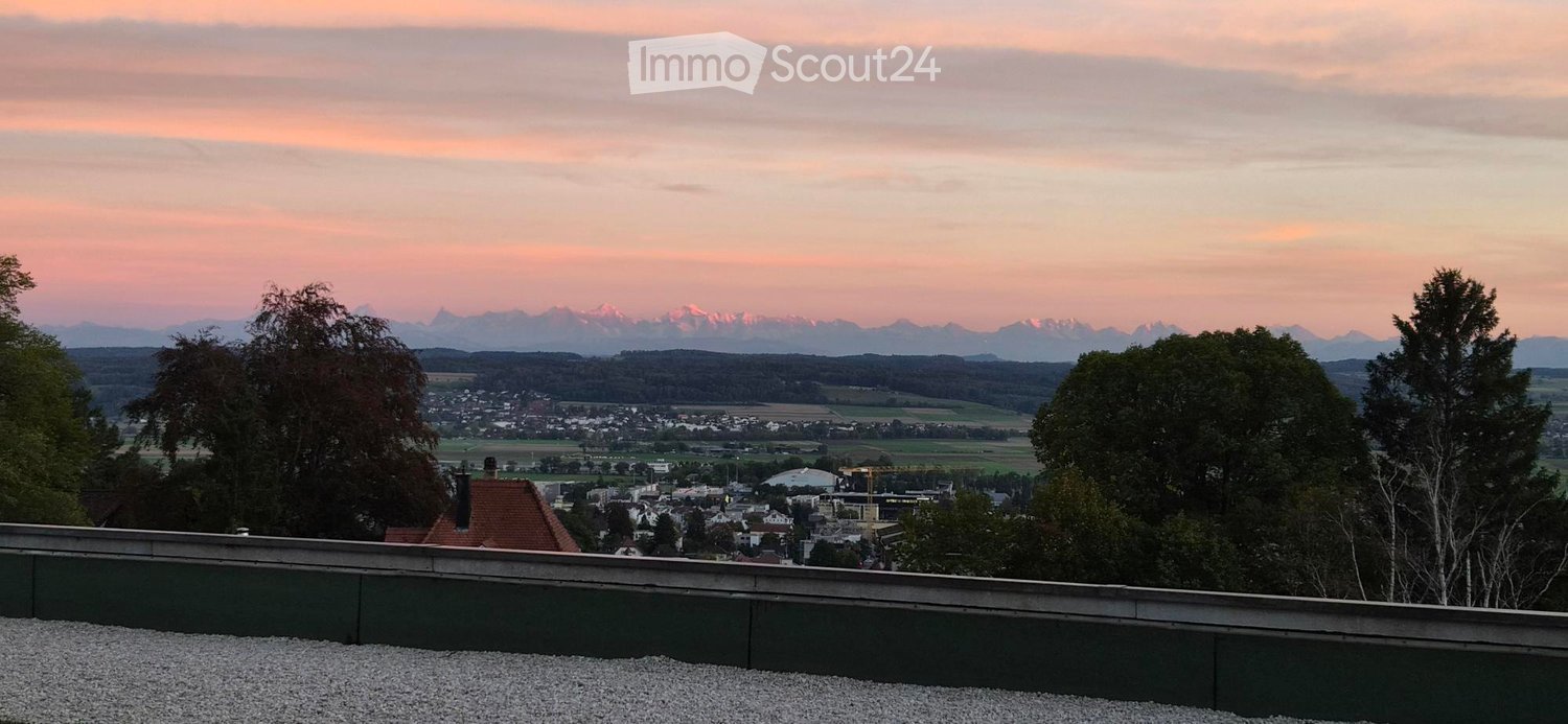 A rooftop terrace with a gravel surface, overlooking a town and distant mountains during sunset.