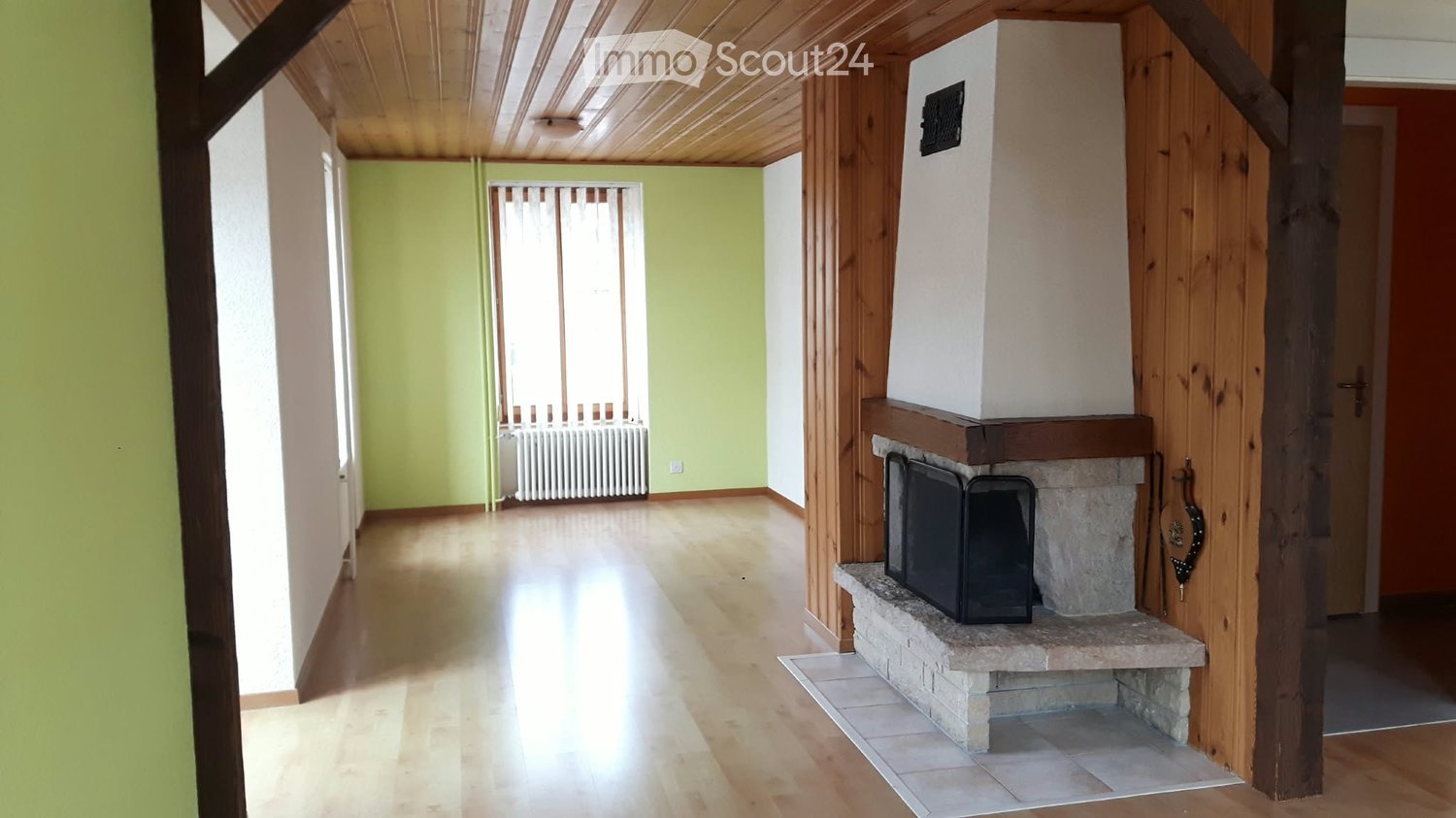 Empty room with wooden flooring, light green walls, and a fireplace with a stone base and wooden mantel.