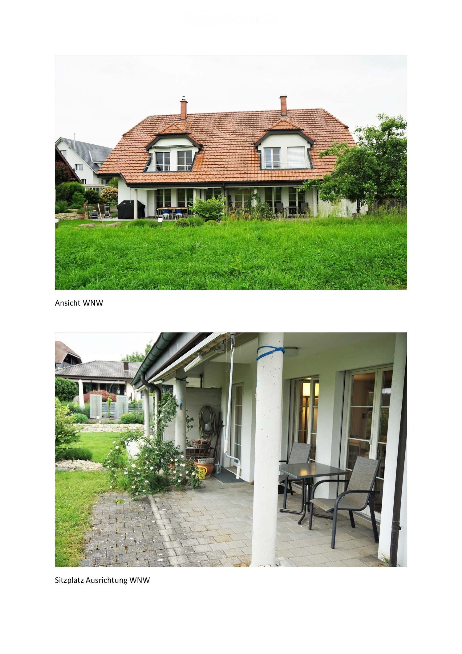 Two-story house with red-tiled roof, white walls, and large windows. The front yard is well-maintained with green grass and some outdoor seating visible near the entrance.