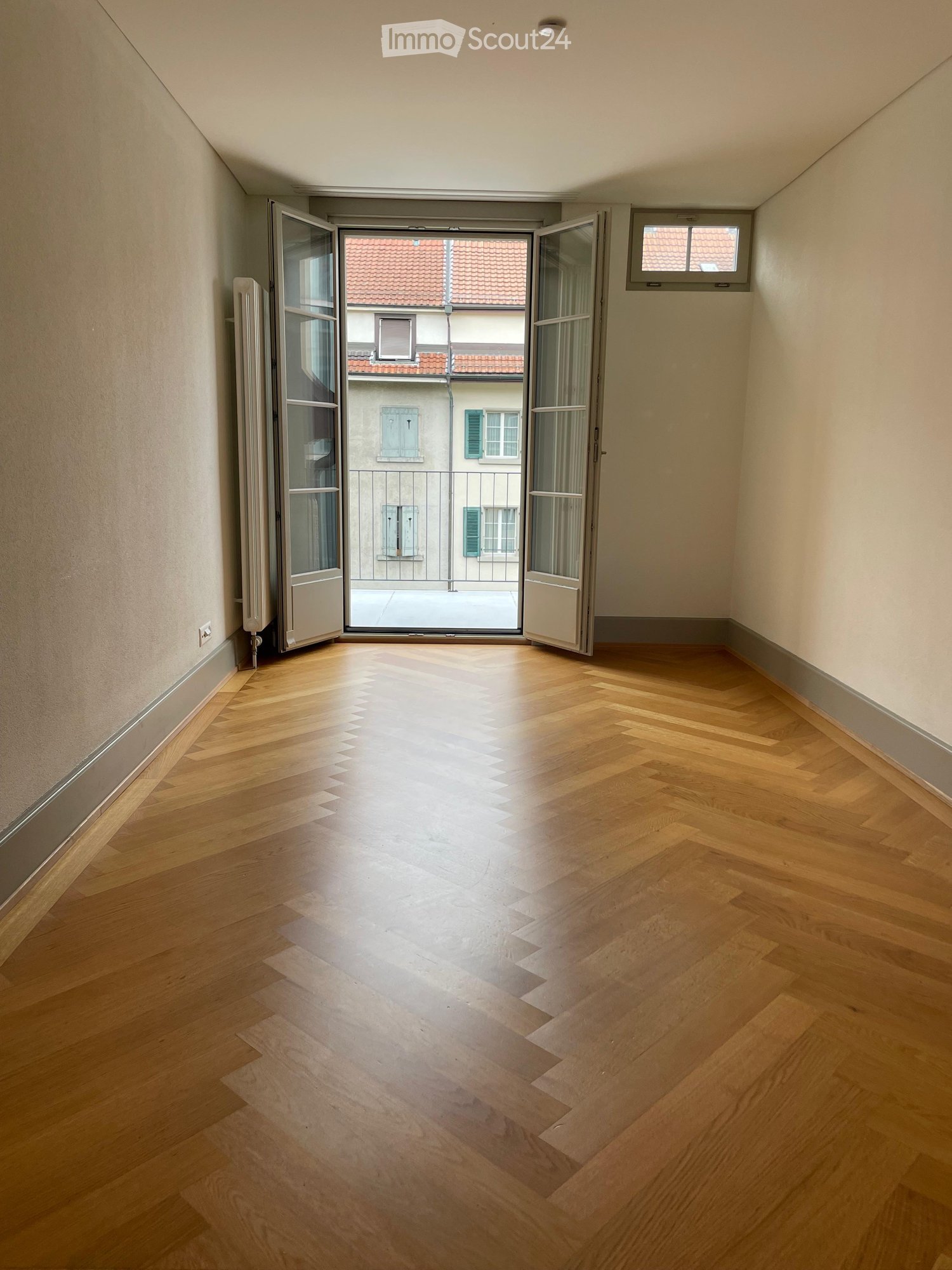 Empty room with wooden flooring, large open doorway leading to a balcony, and visible radiator on the left wall.