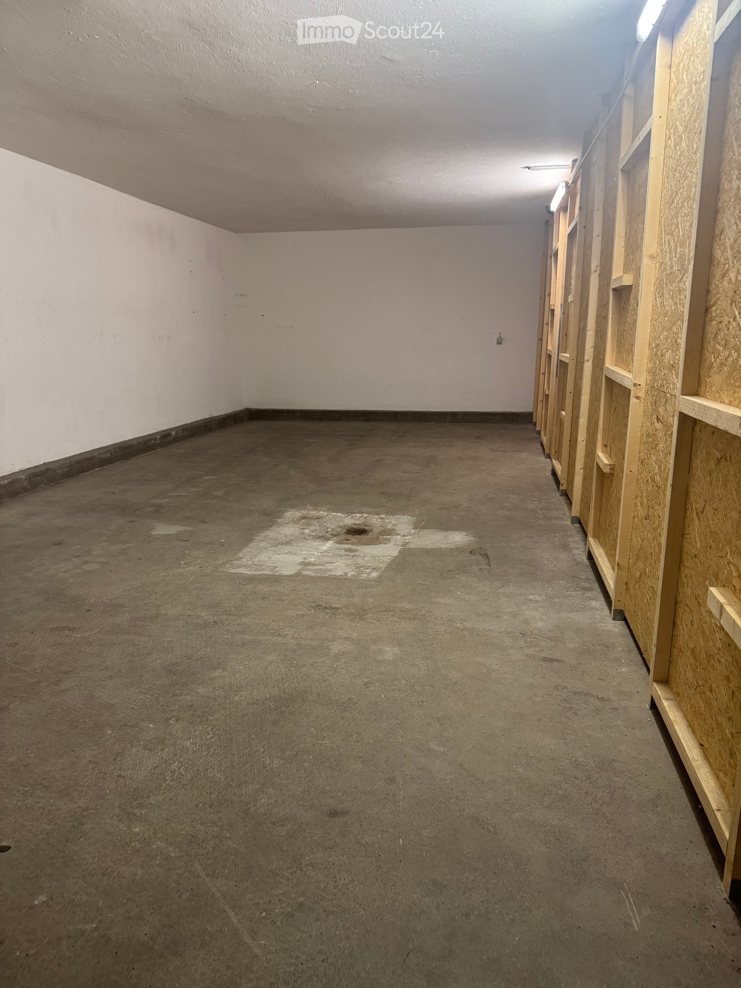 Empty room with concrete floor, white walls, and wooden shelving units on the right side.